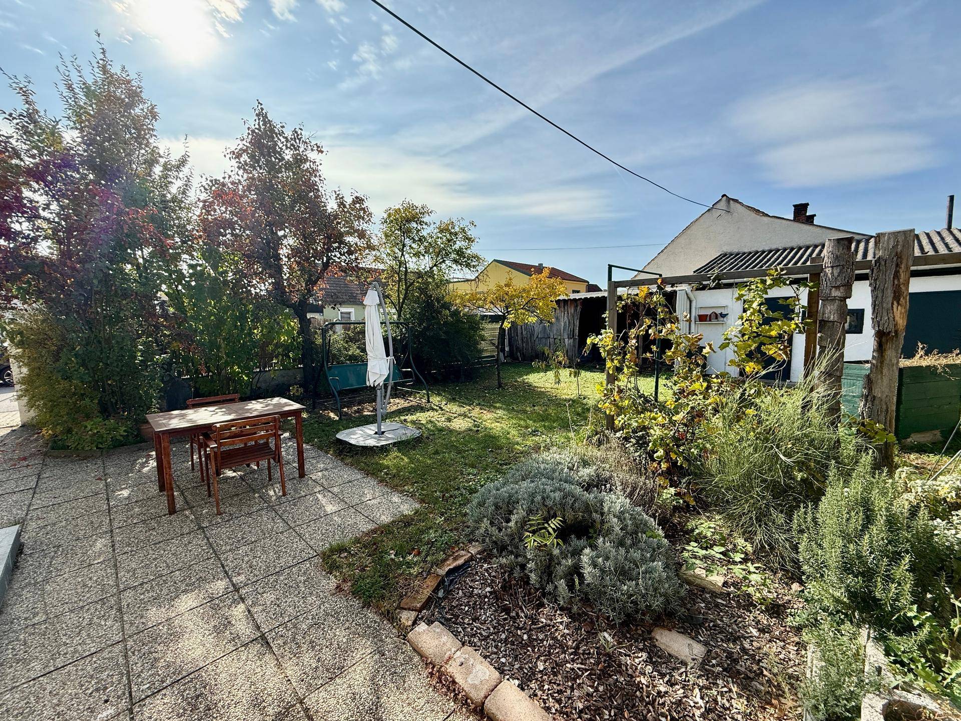 Sonniger Garten mit Terrasse, Rasenfläche und einem Essbereich im Freien.