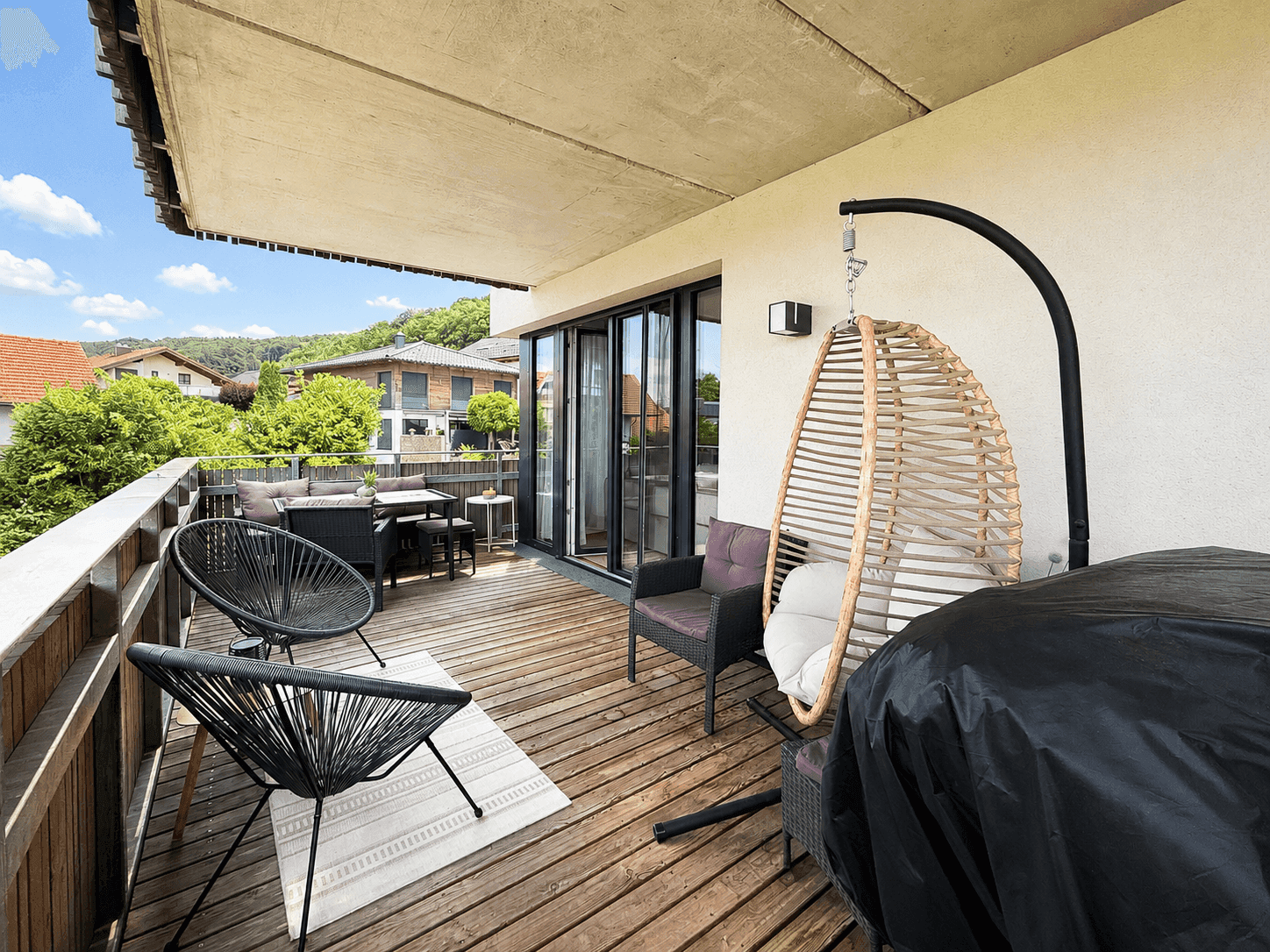 Heller Balkon mit Holzboden, Hängesessel und Blick auf die umliegende Landschaft.