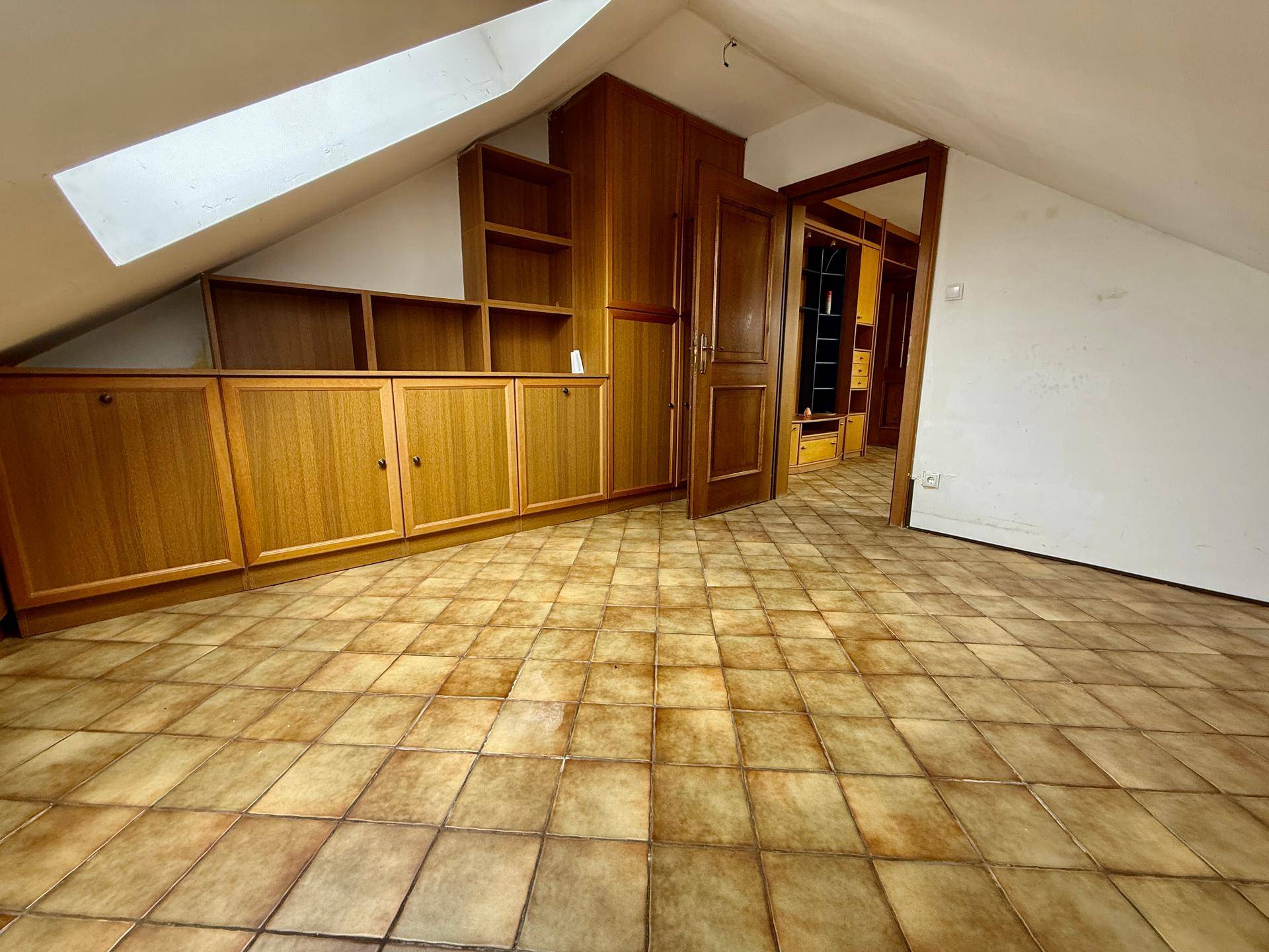 Dachgeschosszimmer mit schrägen Wänden, Einbauschränken und Fliesenboden.