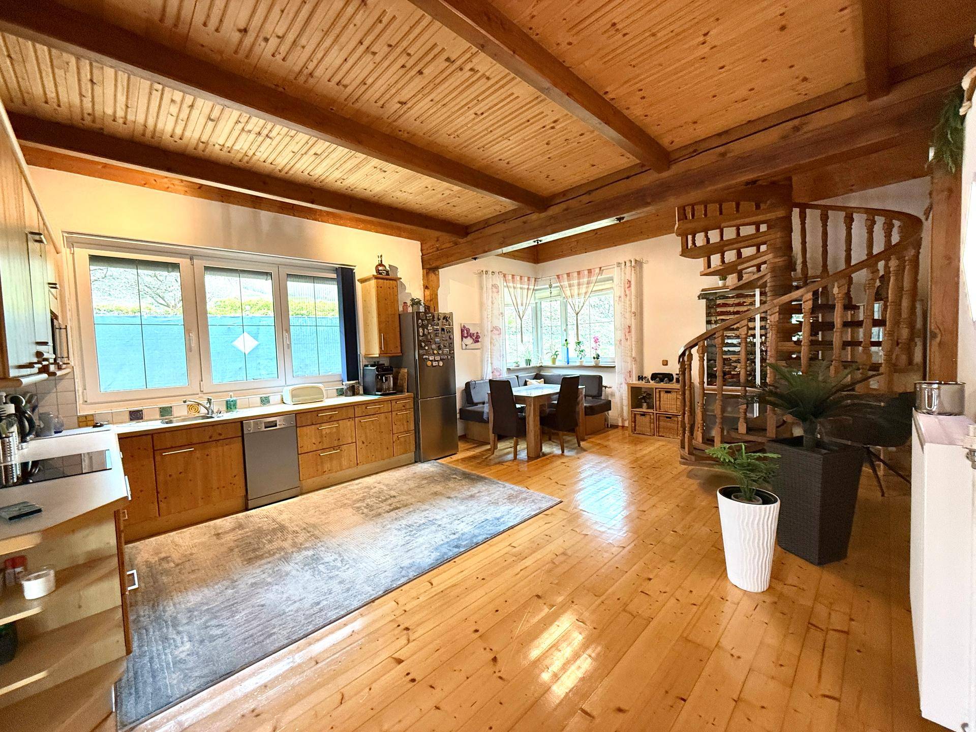 Rustikale Wohnküche mit Holzboden, Essecke und Wendeltreppe zum Obergeschoss.