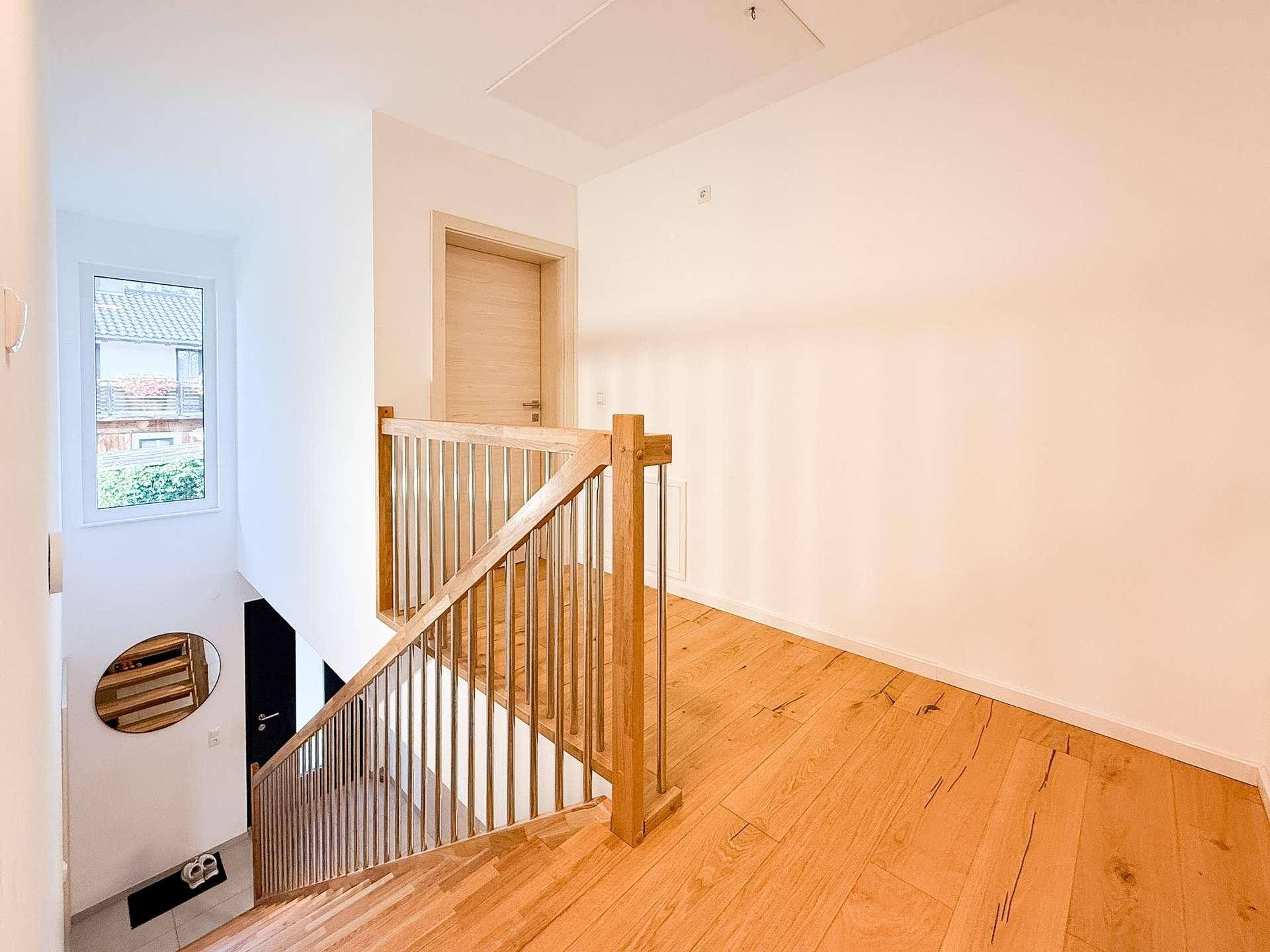 Heller Flur mit Holztreppe, Holzboden und natürlichem Lichteinfall durch ein Fenster.