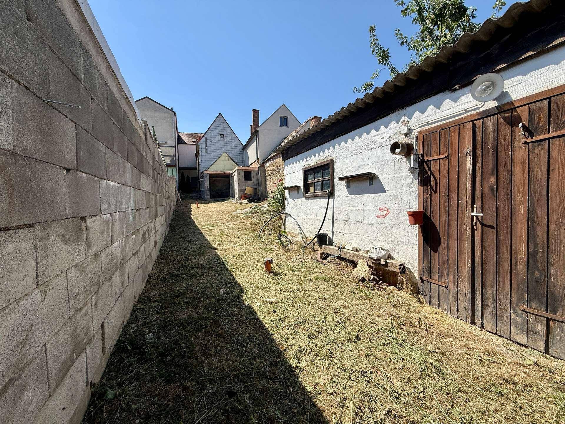 Länglicher Gartenbereich im Hinterhof, umgeben von Gebäuden und Mauern.