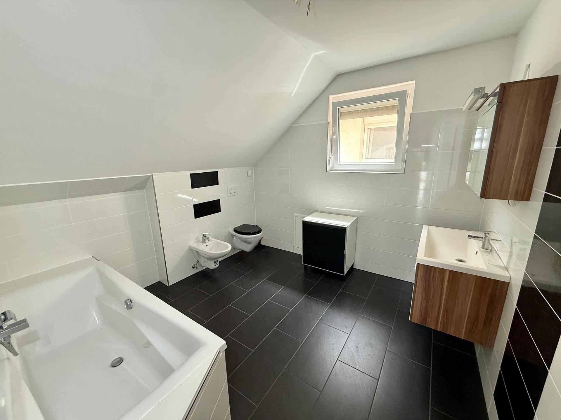 Modernes Badezimmer mit Badewanne, Bidet, Waschtisch und Fenster unter Dachschräge.