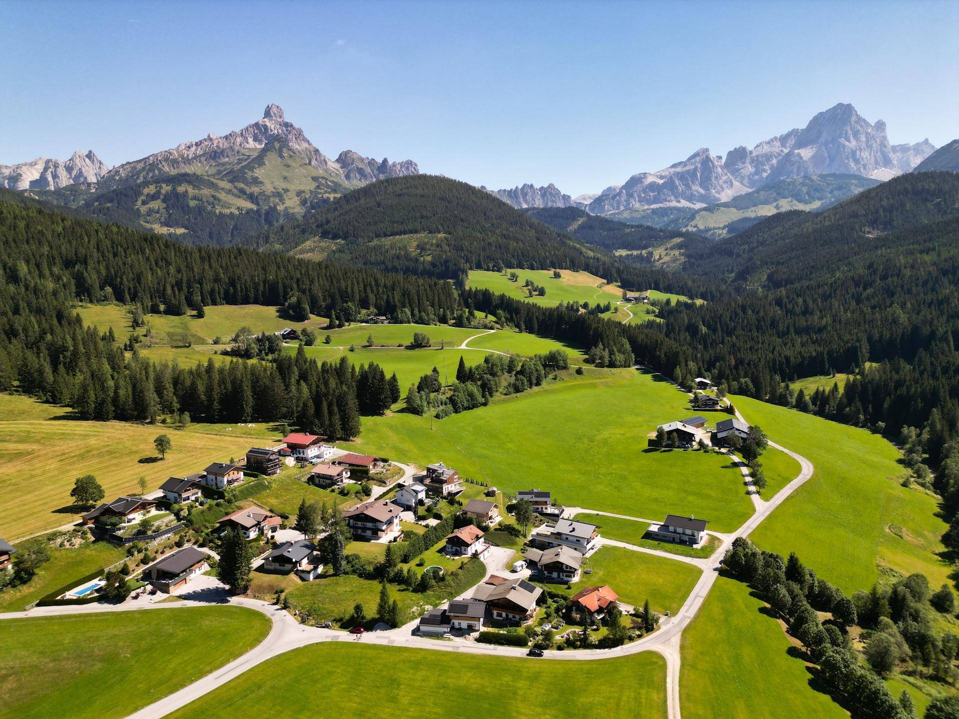 Malerische Luftaufnahme eines Dorfes in einem grünen Tal, umgeben von majestätischen Bergen.