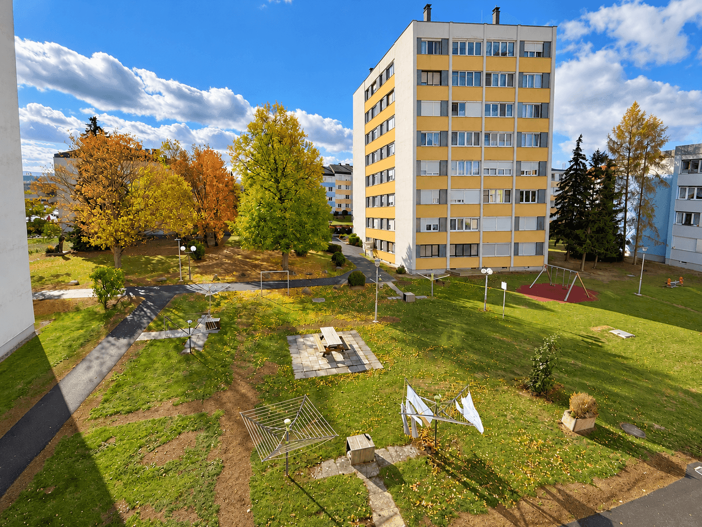 Weitläufige Wohnanlage mit Grünflächen, Spielplatz und Mehrfamilienhäusern unter blauem Himmel.