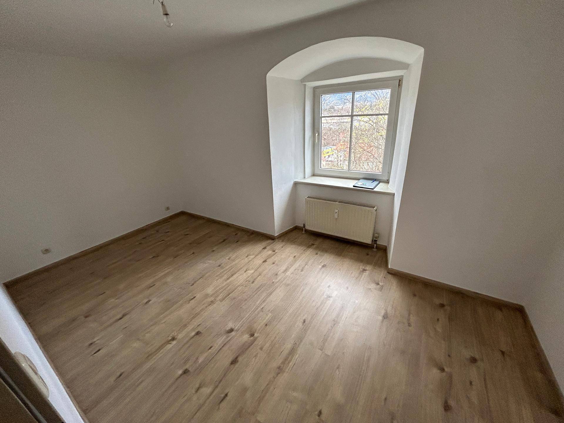 Helles Schlafzimmer mit Laminatboden und einem charmanten Bogenfenster, das viel Tageslicht hereinlässt.