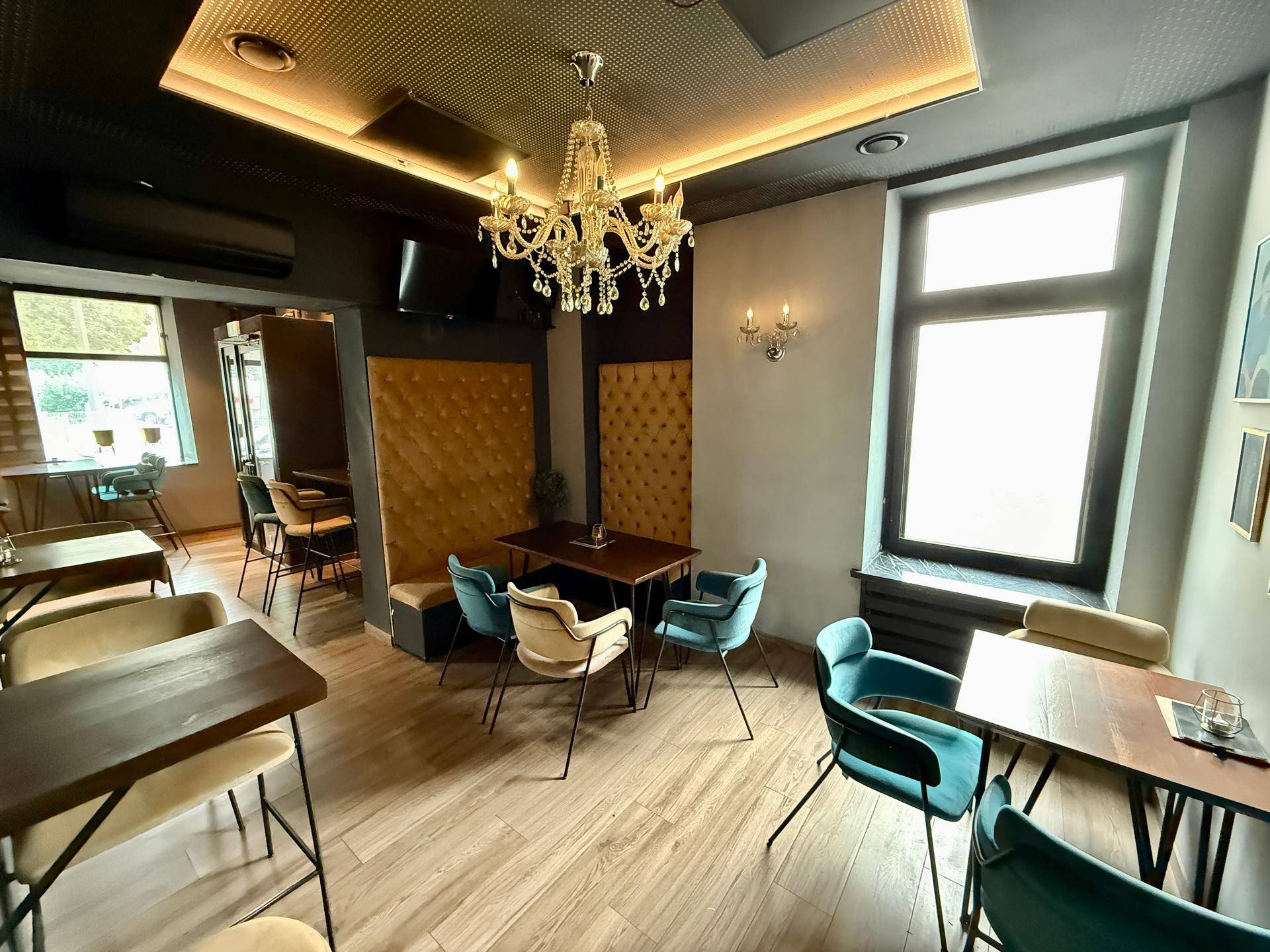 Gemütlicher Sitzbereich der Bar mit gepolsterten Wänden, Tischen und Stühlen unter einem Kronleuchter.
