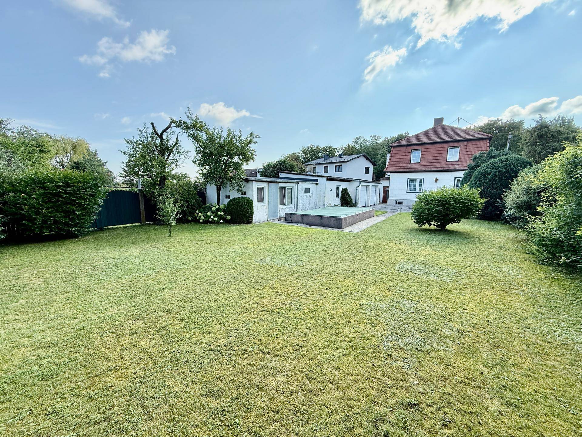 Großer, gepflegter Garten mit Rasenfläche, kleinem Pool und Nebengebäuden.