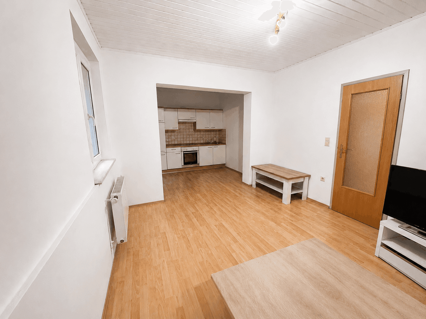 Wohnzimmer mit Laminatboden und Zugang zu einer kleinen Küchenzeile, ideal für offenes Wohnen.