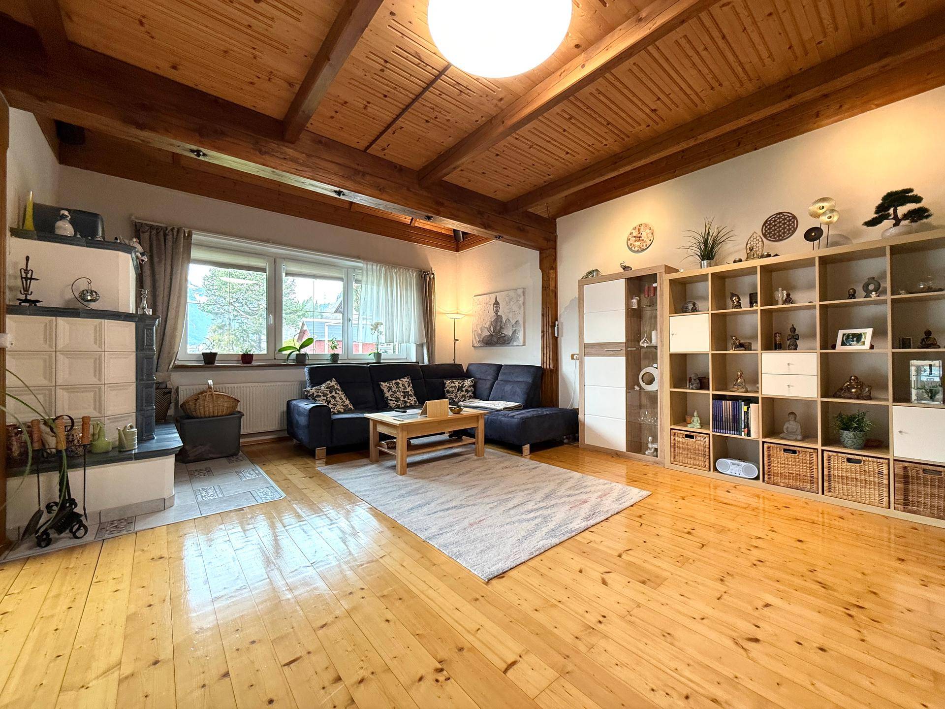 Gemütliches Wohnzimmer mit Holzbalkendecke, Kachelofen und Blick ins Grüne.