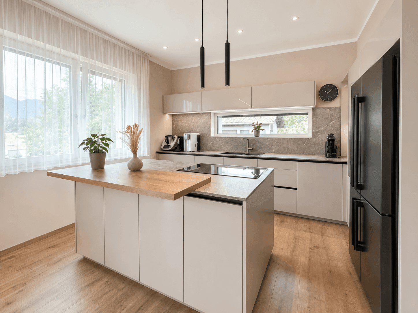 Moderne Küche mit Kücheninsel, Induktionskochfeld und Blick ins Grüne durch das Fenster.
