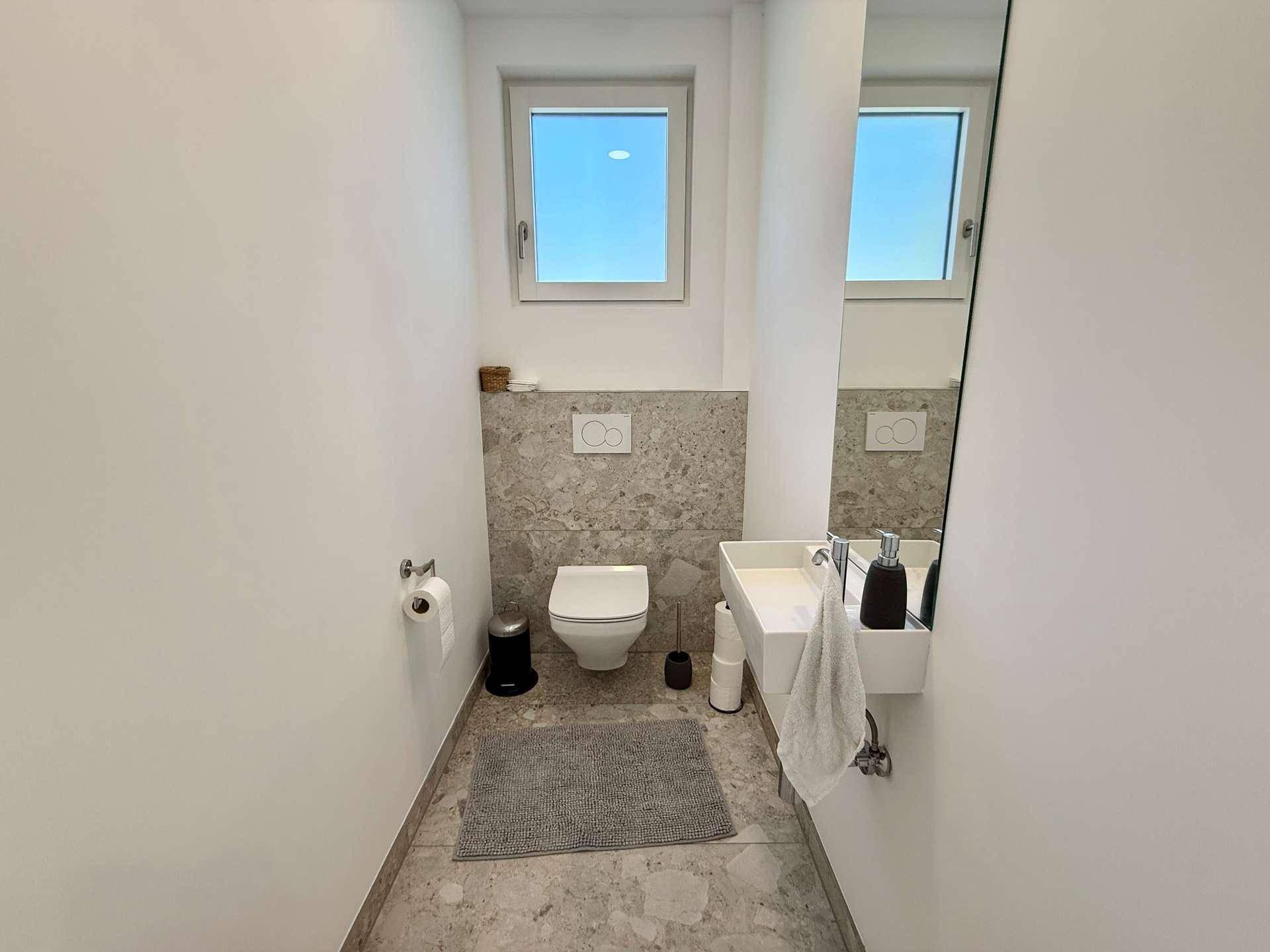 Modernes Gäste-WC mit Fenster, Wand-WC und kleinem Waschbecken.
