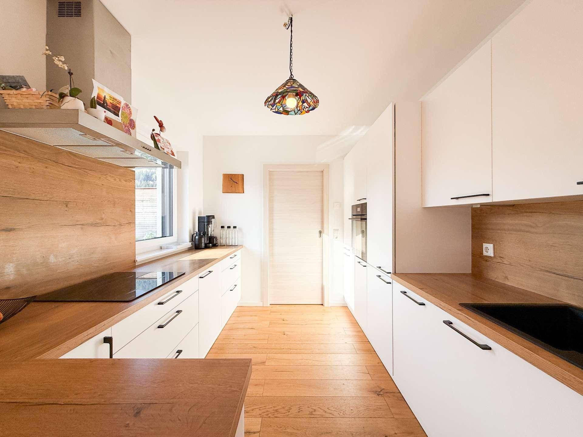 Helle Einbauküche mit weißen Fronten, Holz-Arbeitsplatten und modernen Geräten.