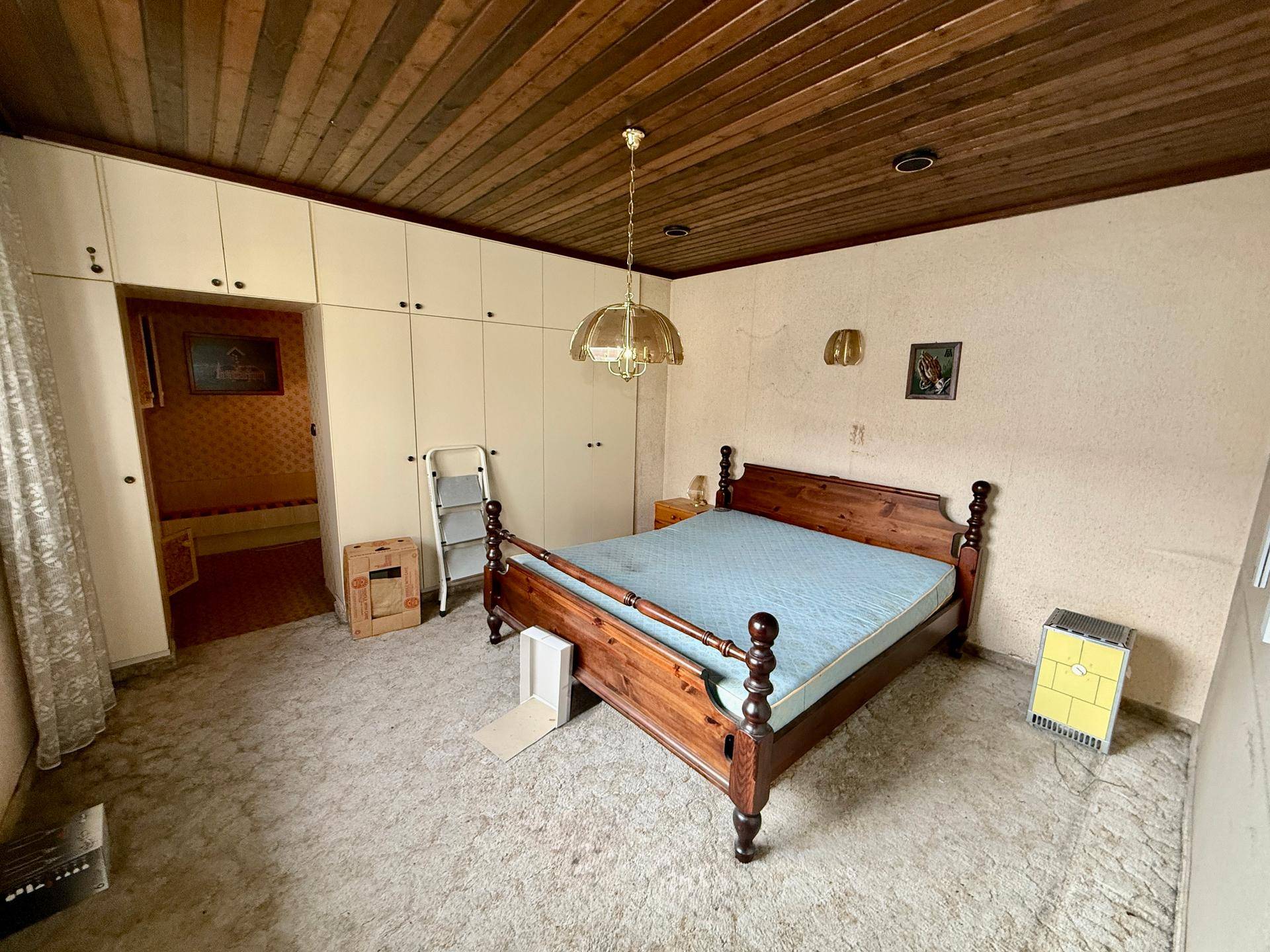 Schlafzimmer mit Holzbett, Einbauschränken und Teppichboden unter einer Holzdecke.