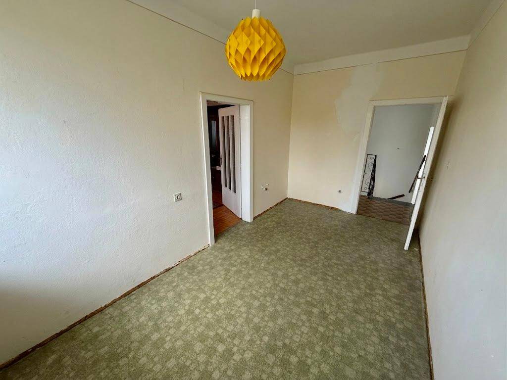 Renovierungsbedürftiger Raum mit gemustertem Teppichboden und zwei Türen.