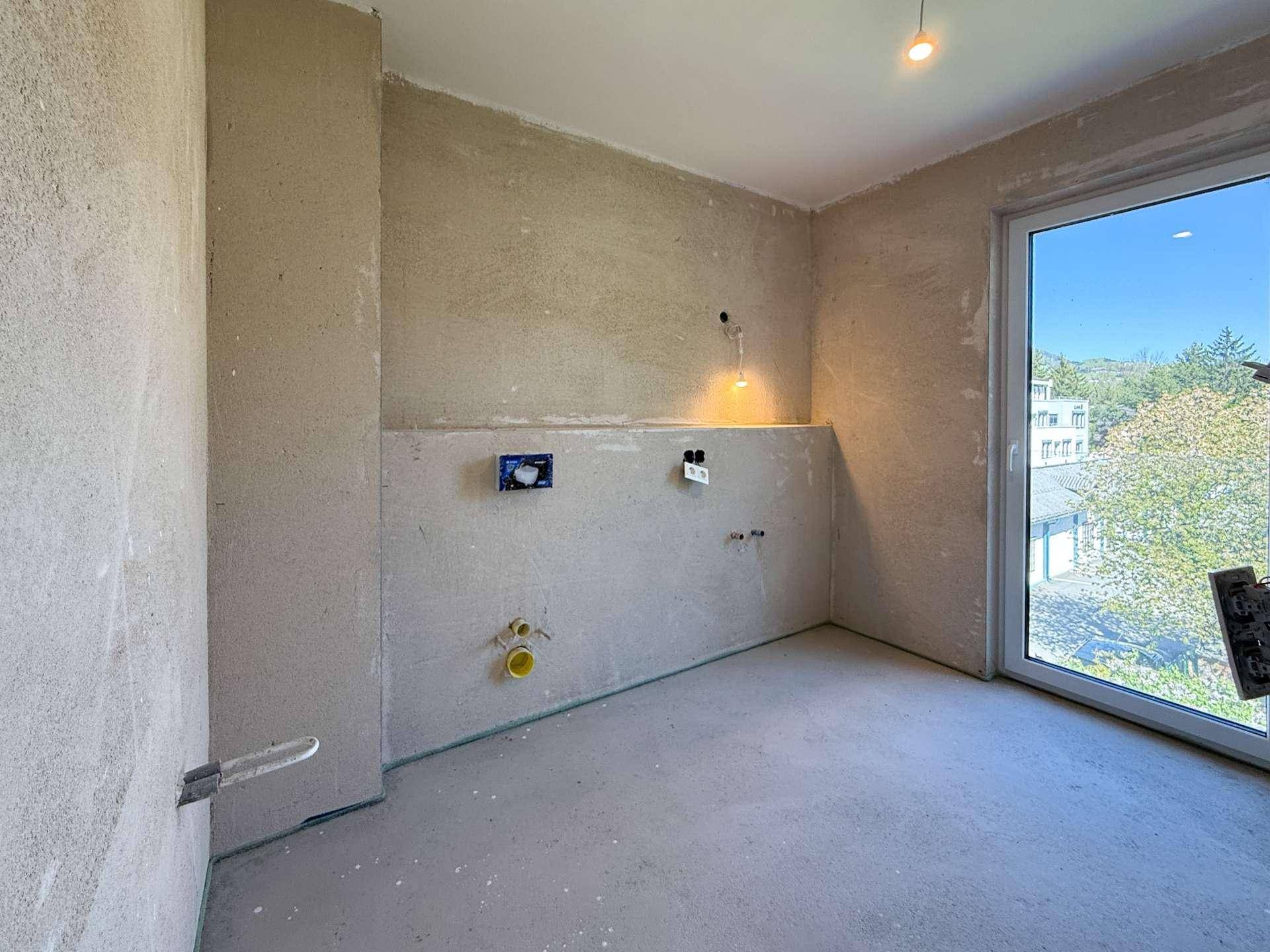 Badezimmer im Rohbau mit Fenster und vorbereiteten Anschlüssen für Sanitäranlagen.