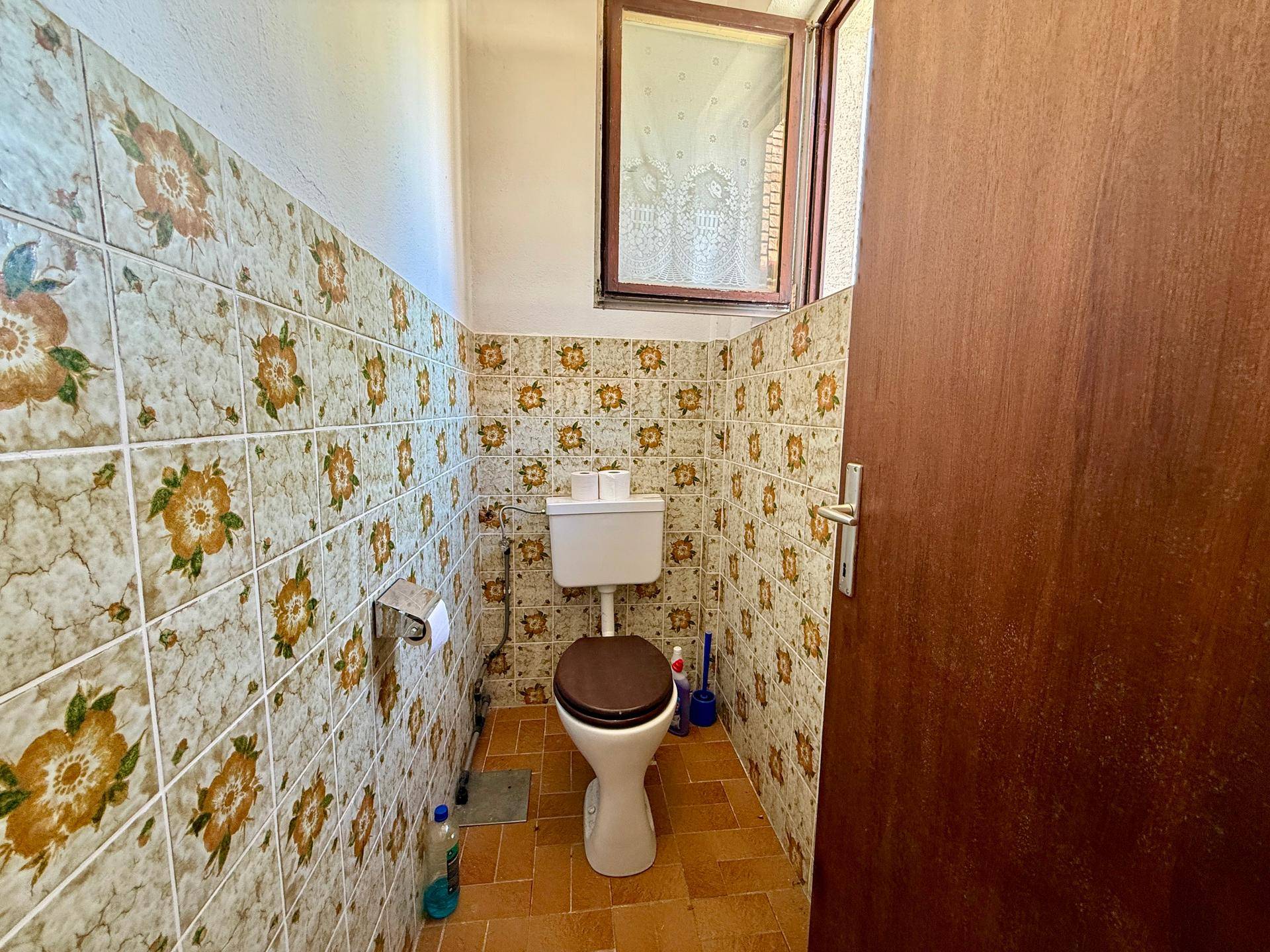 Separate Toilette mit floralen Fliesen und kleinem Fenster für natürliche Belüftung.
