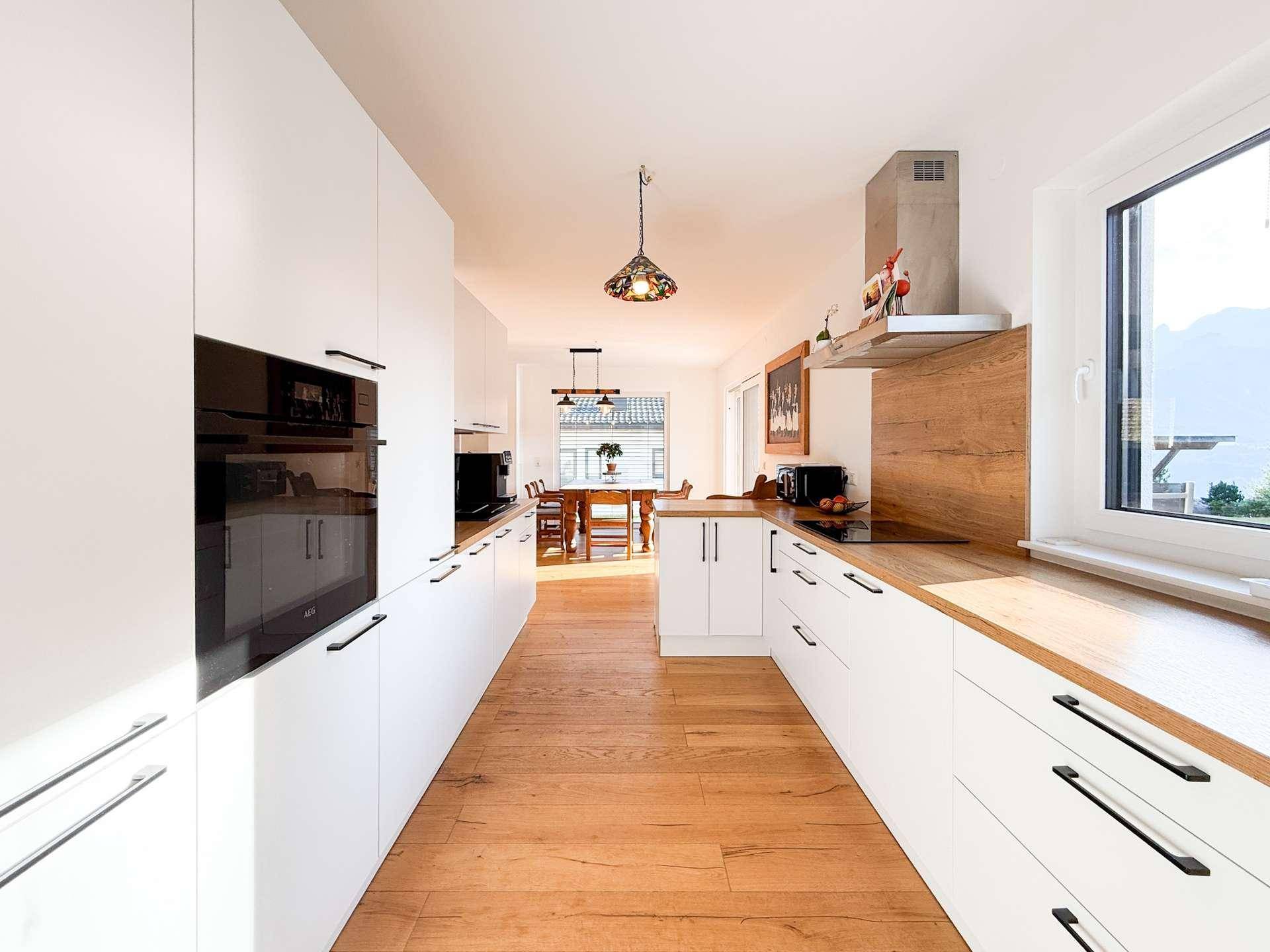 Lange Küche mit weißen Schränken, Holz-Arbeitsplatten und Blick in den Essbereich.