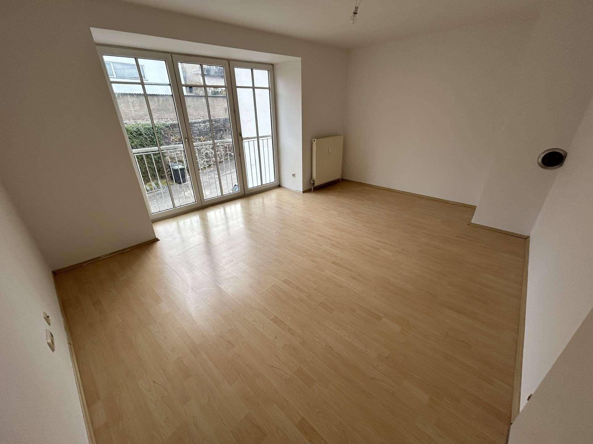 Heller Wohnraum mit Laminatboden und großen Fenstern, die auf einen französischen Balkon führen.