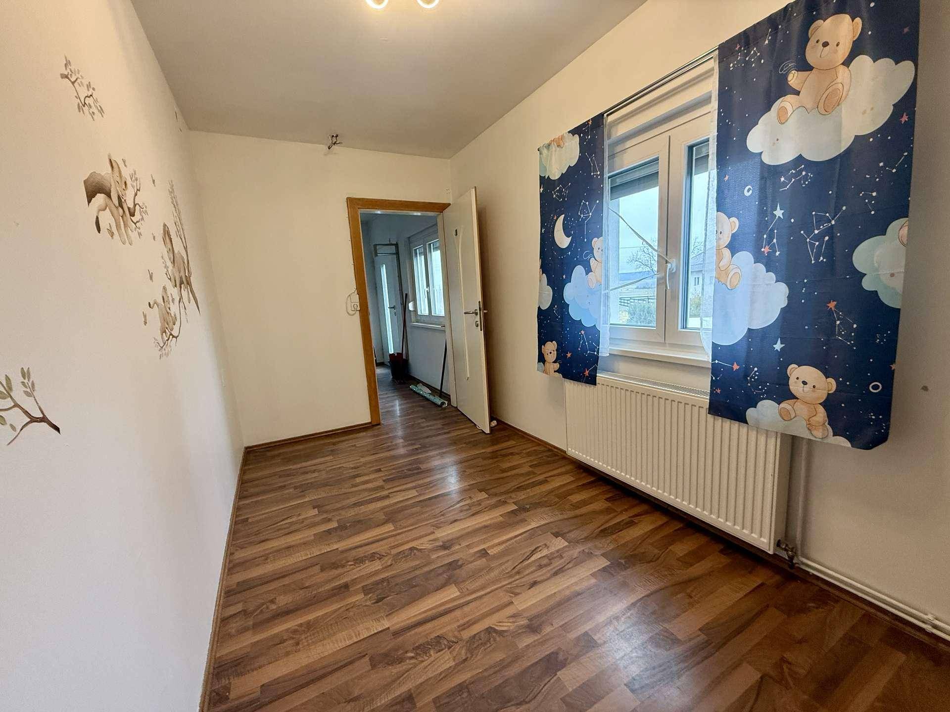 Kinderzimmer mit Holzboden, Fenster und verspielten Vorhängen mit Bärenmotiven.