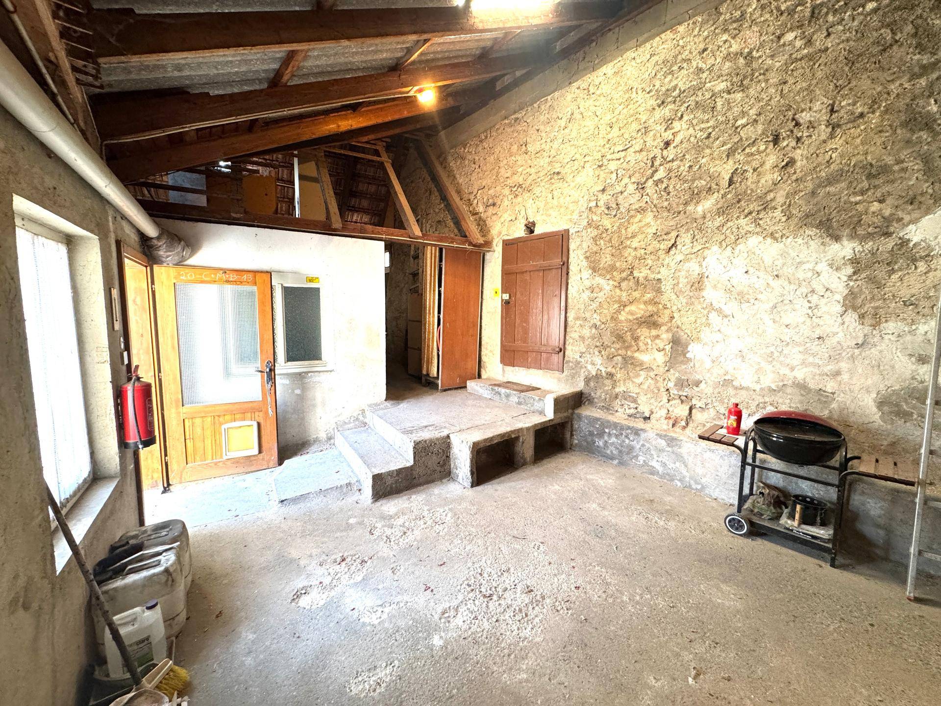 Rustikaler Scheunenbereich mit Steinwänden, Holzbalken und Betonboden.