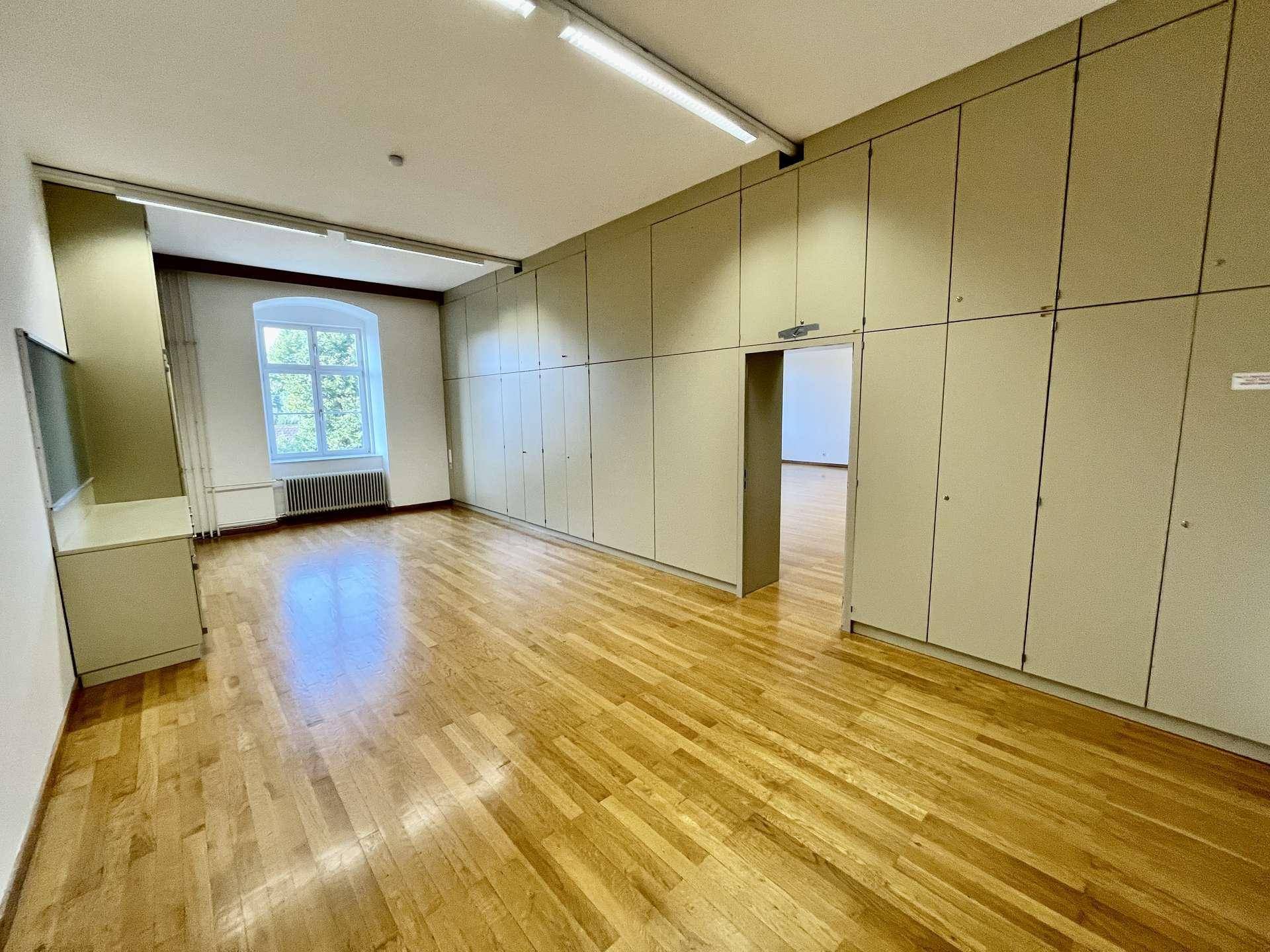 Großer Raum mit Holzboden, Einbauschränken entlang einer Wand und einem Fenster.