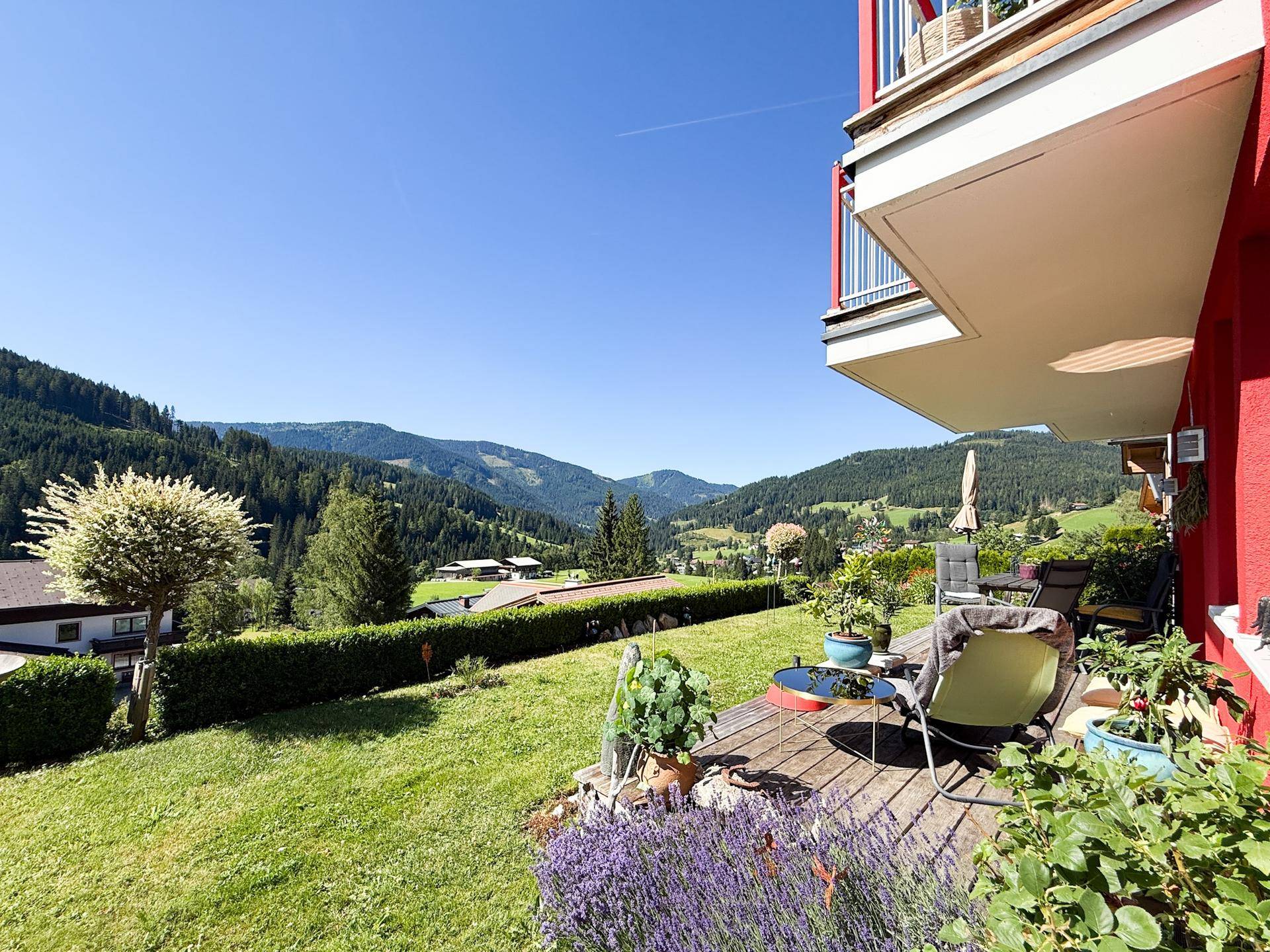 Sonniger Terrassenbereich mit Gartenmöbeln und weitem Blick auf die grüne Berglandschaft.