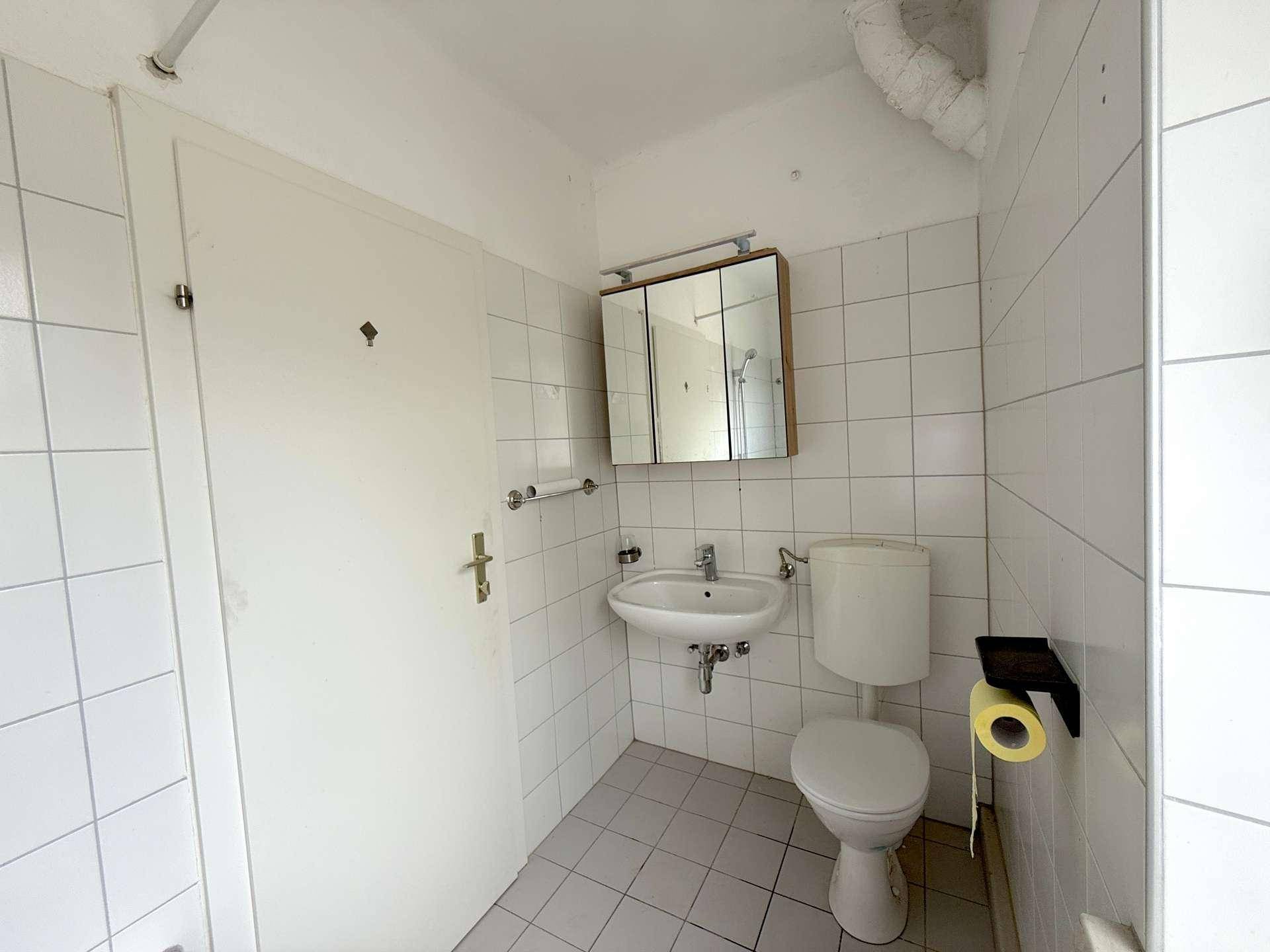 Kleines WC mit weißen Fliesen, Waschbecken und Spiegelschrank.