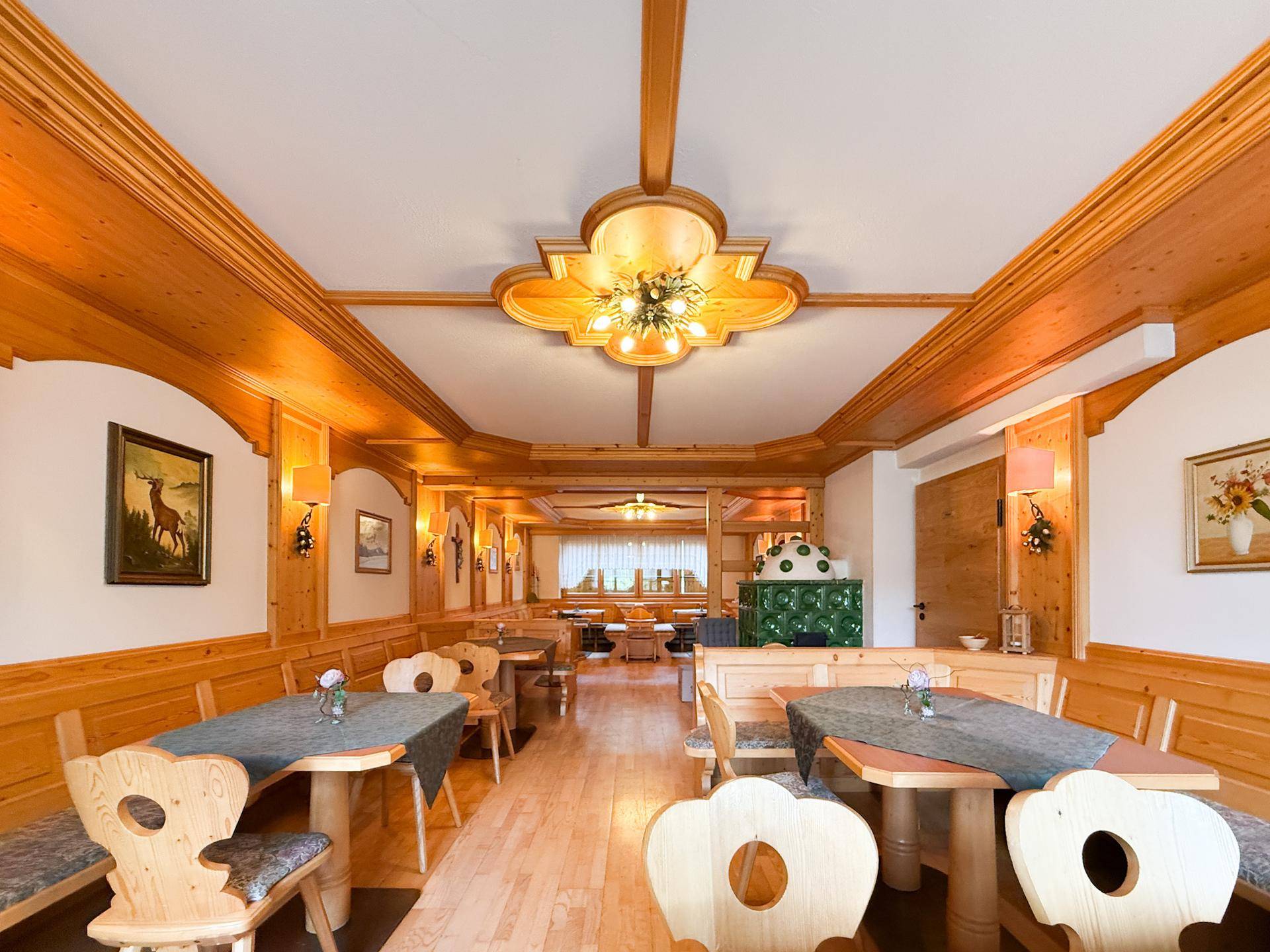 Gemütlicher Speisesaal im Landhausstil mit viel Holzvertäfelung, Kachelofen und traditionellen Möbeln.