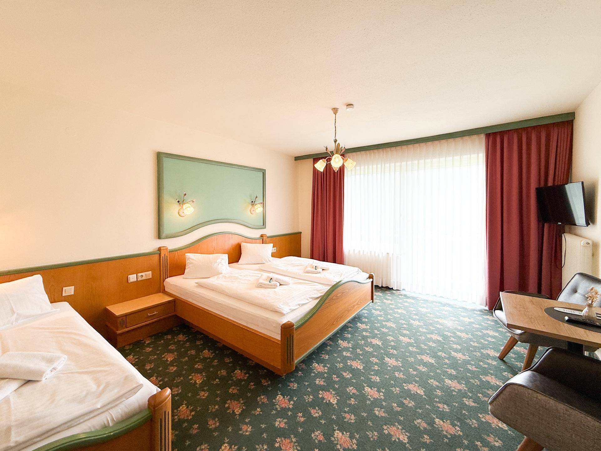 Helles Schlafzimmer mit zwei Einzelbetten, Teppichboden und Zugang zu einem Balkon.