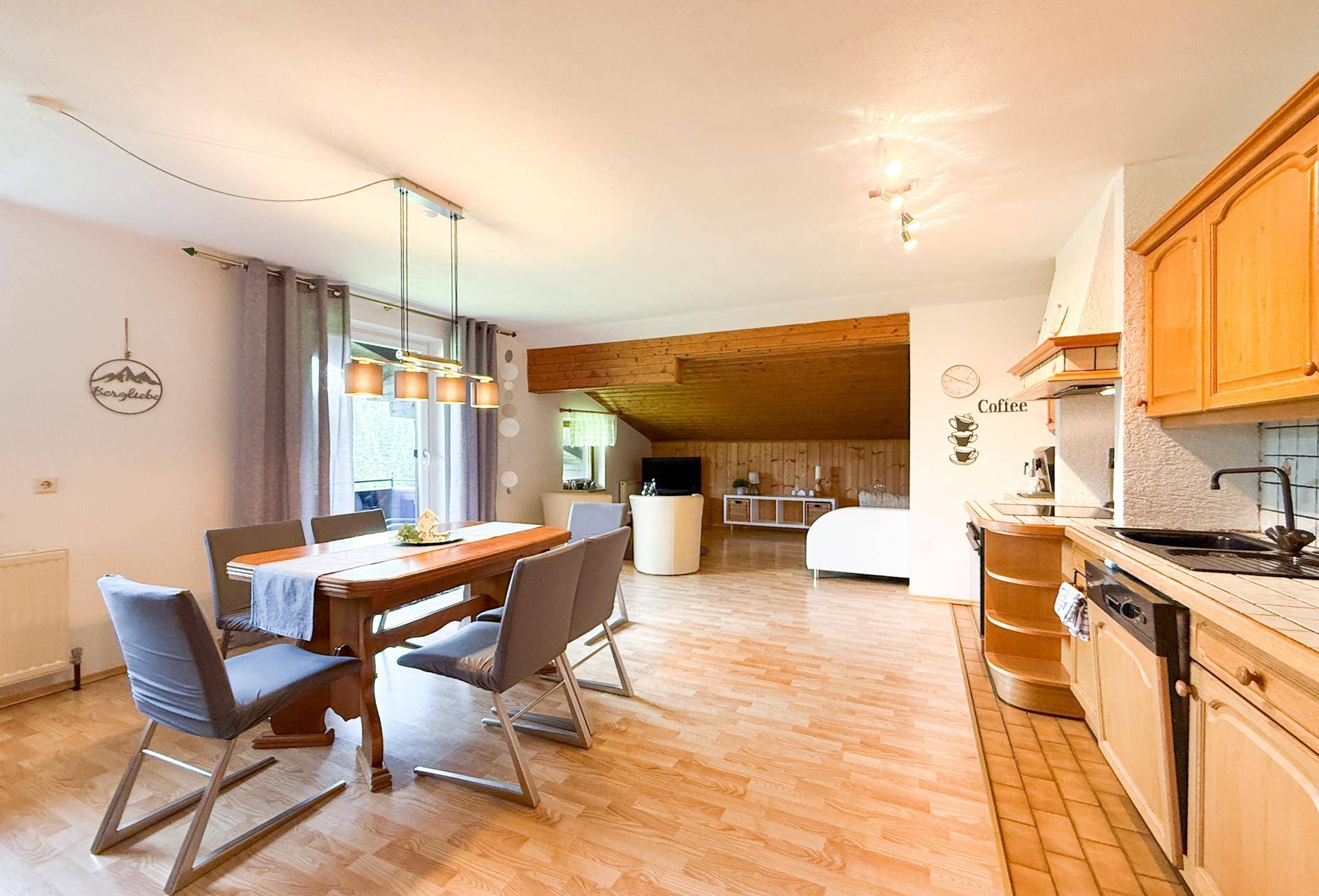 Offener Wohn-Essbereich mit integrierter Küche, Holzboden und Zugang zum Balkon.