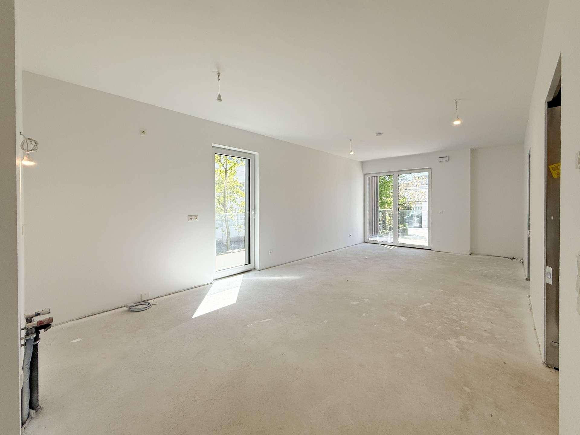 Heller, unmöblierter Wohnraum im Rohbauzustand mit großen Fenstern und viel Tageslicht.