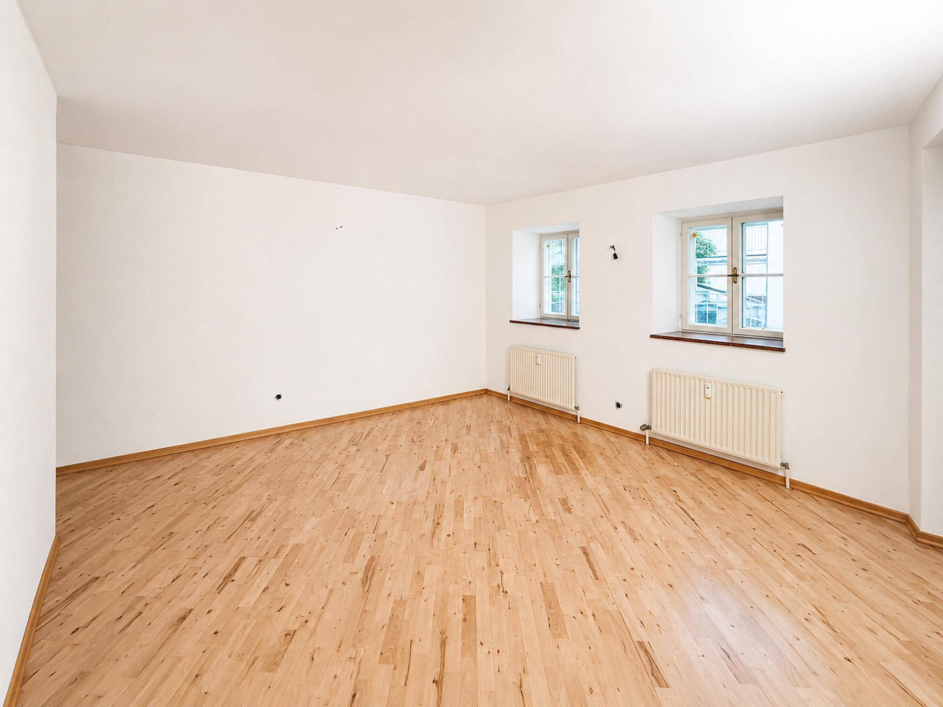 Heller Raum mit zwei Fenstern und klassischem Holzboden, ideal als Wohn- oder Schlafzimmer.