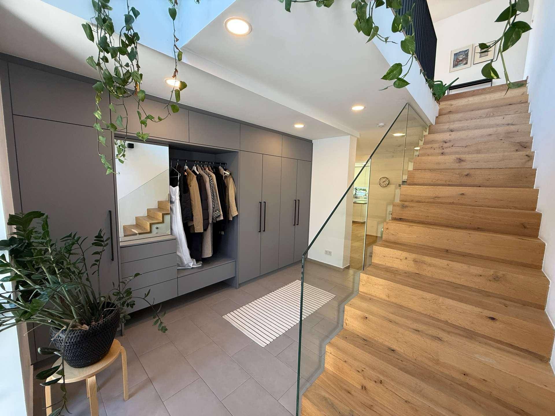 Heller Eingangsbereich mit moderner Garderobe, Holztreppe und Glasgeländer.