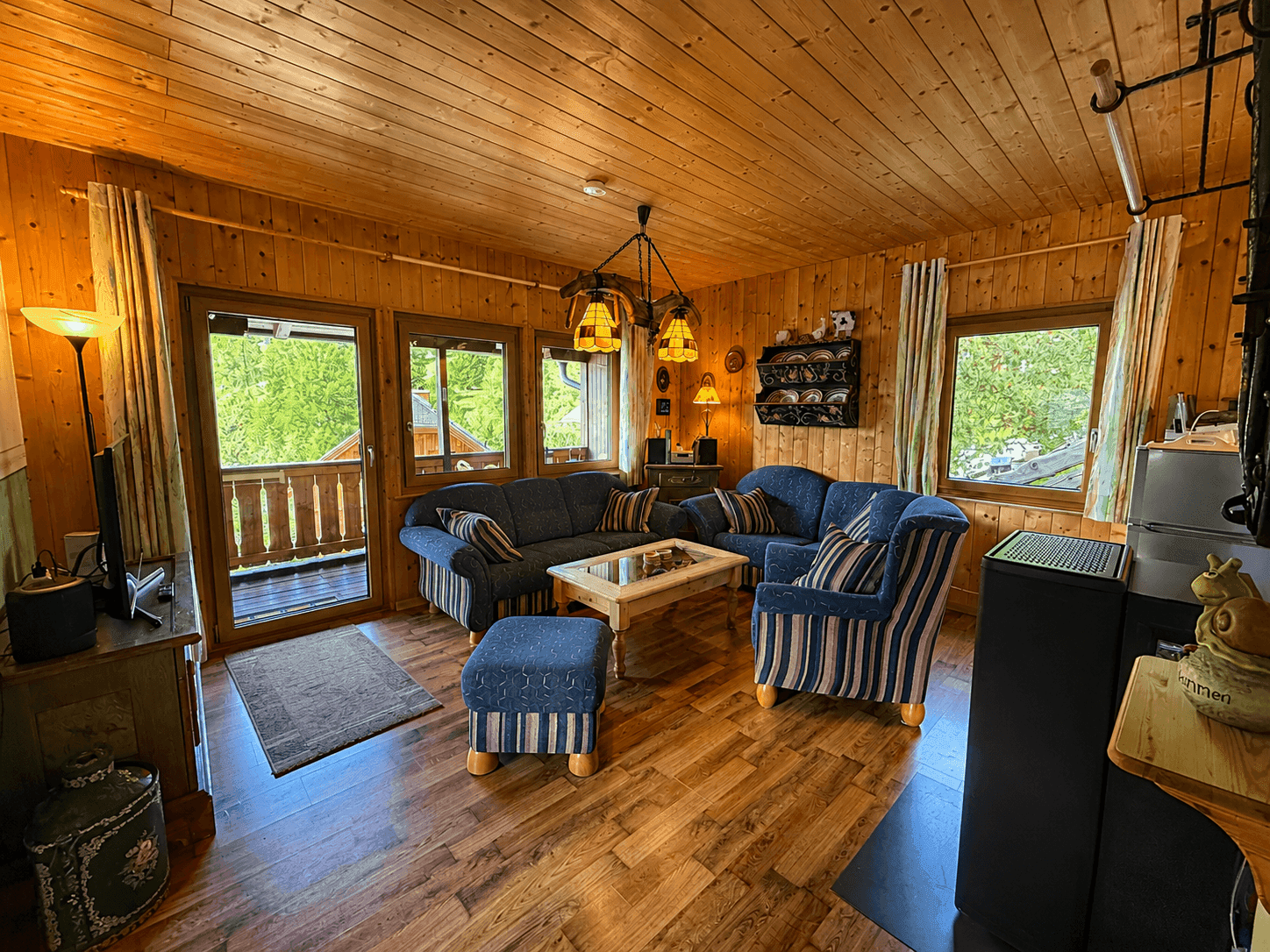 Rustikales Wohnzimmer mit Holzvertäfelung, blauen Sofas und Zugang zum Balkon.