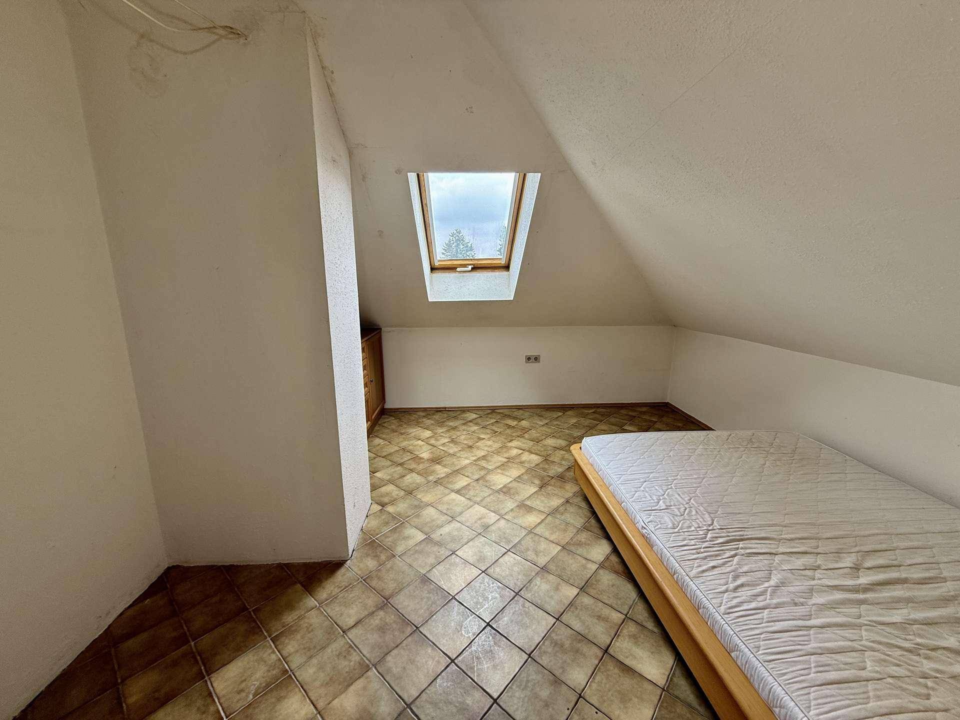 Helles Schlafzimmer im Dachgeschoss mit Dachfenster und Fliesenboden.