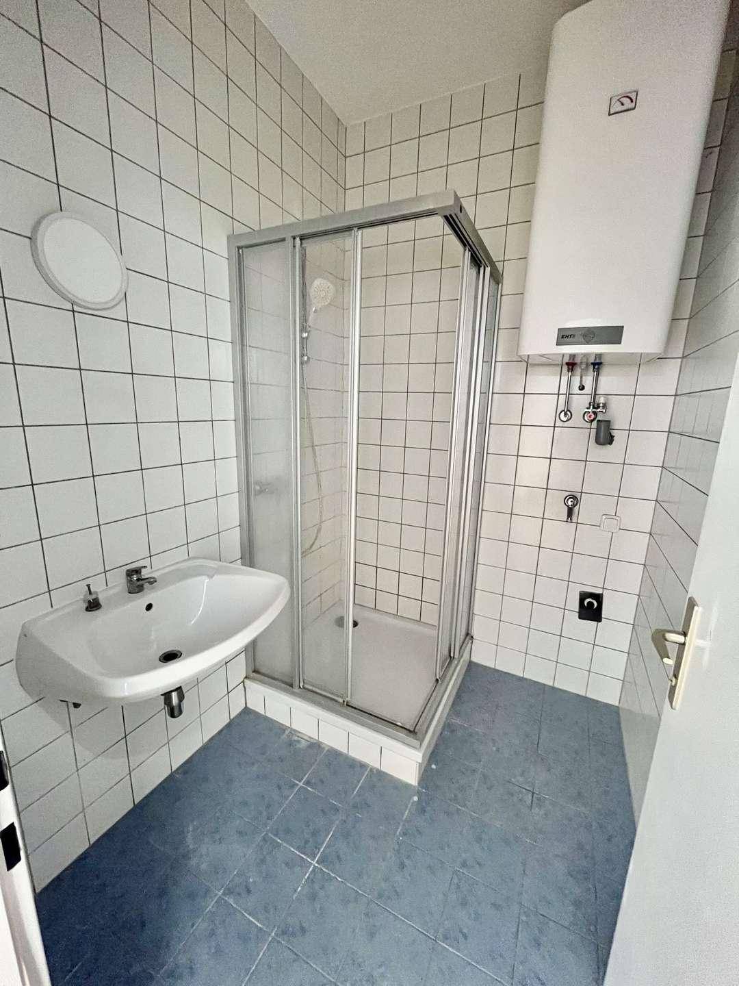 Funktionales Badezimmer mit Duschkabine, Waschbecken und weiß gefliesten Wänden, sauber und hell.