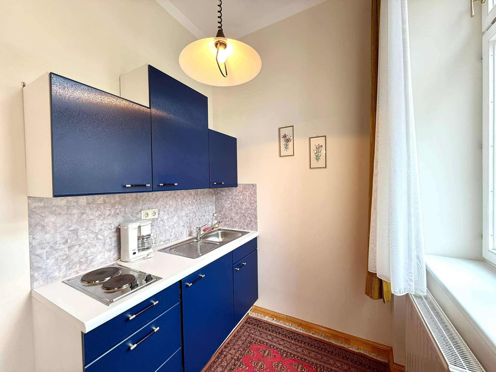 Funktionale Küchenzeile mit blauen Schränken, Kochfeld und Spüle, ideal für kleine Wohnbereiche.