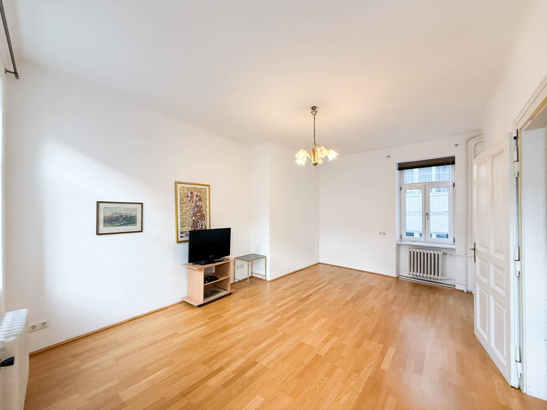 Geräumiges, unmöbliertes Wohnzimmer mit Holzboden und zwei Fenstern.