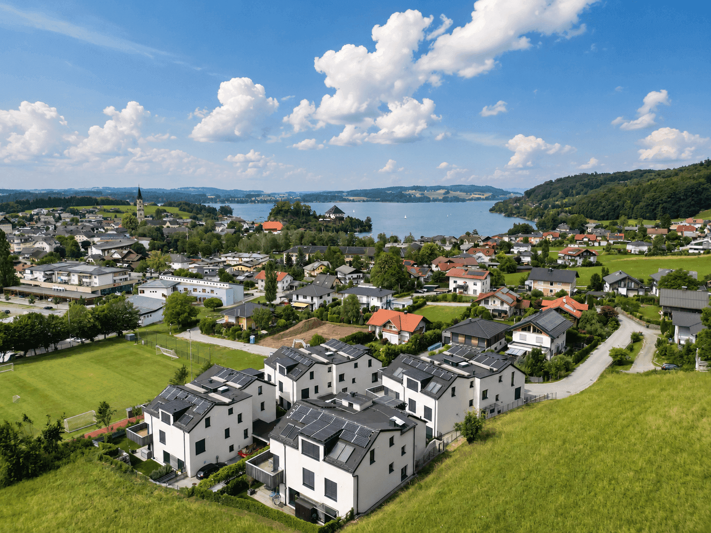 Luftaufnahme einer Wohnsiedlung am Seeufer mit umliegender Natur und Bergen.