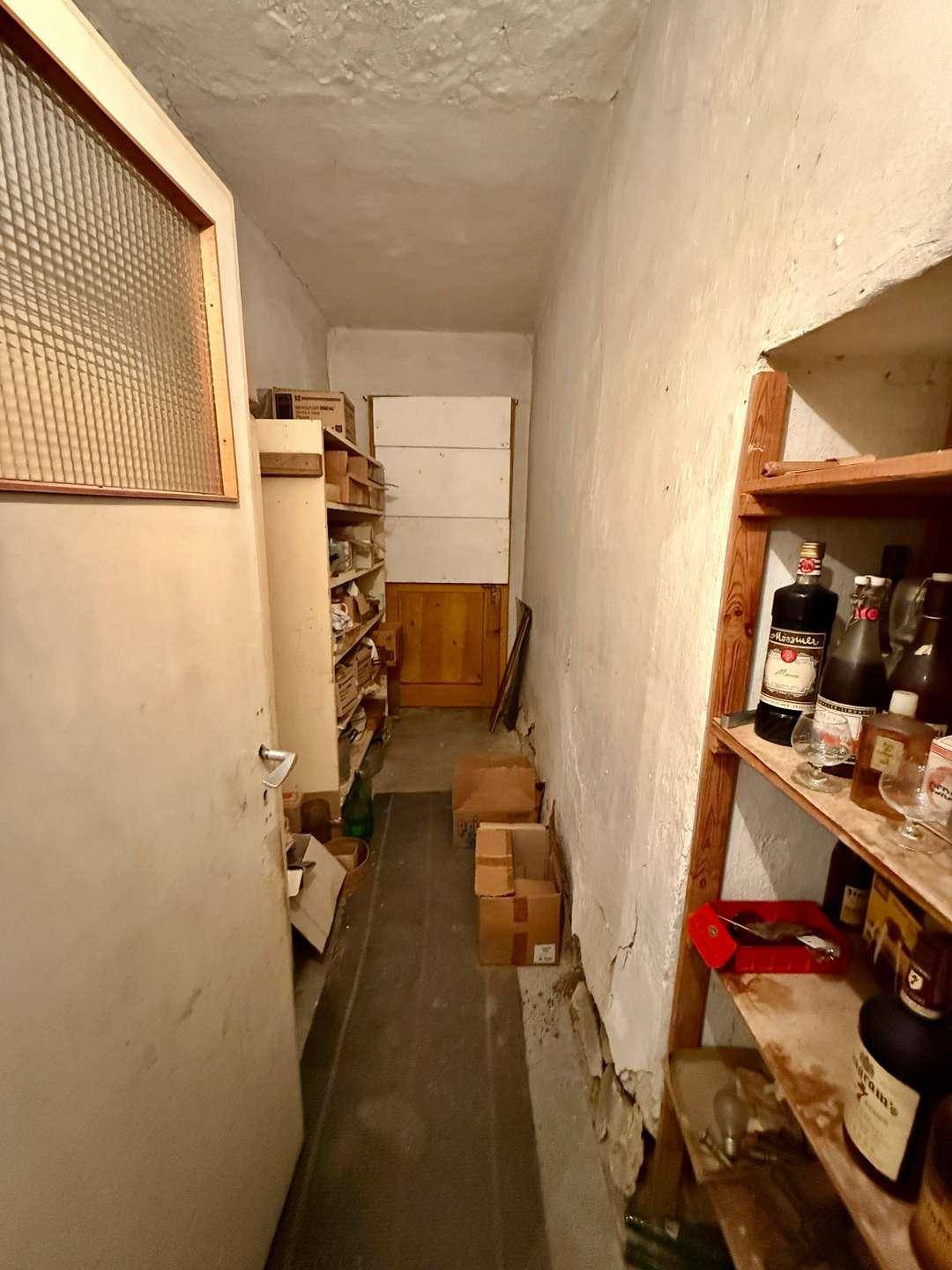 Schmaler Vorratsraum mit Regalen voller Flaschen und Kartons, ideal zur Lagerung.