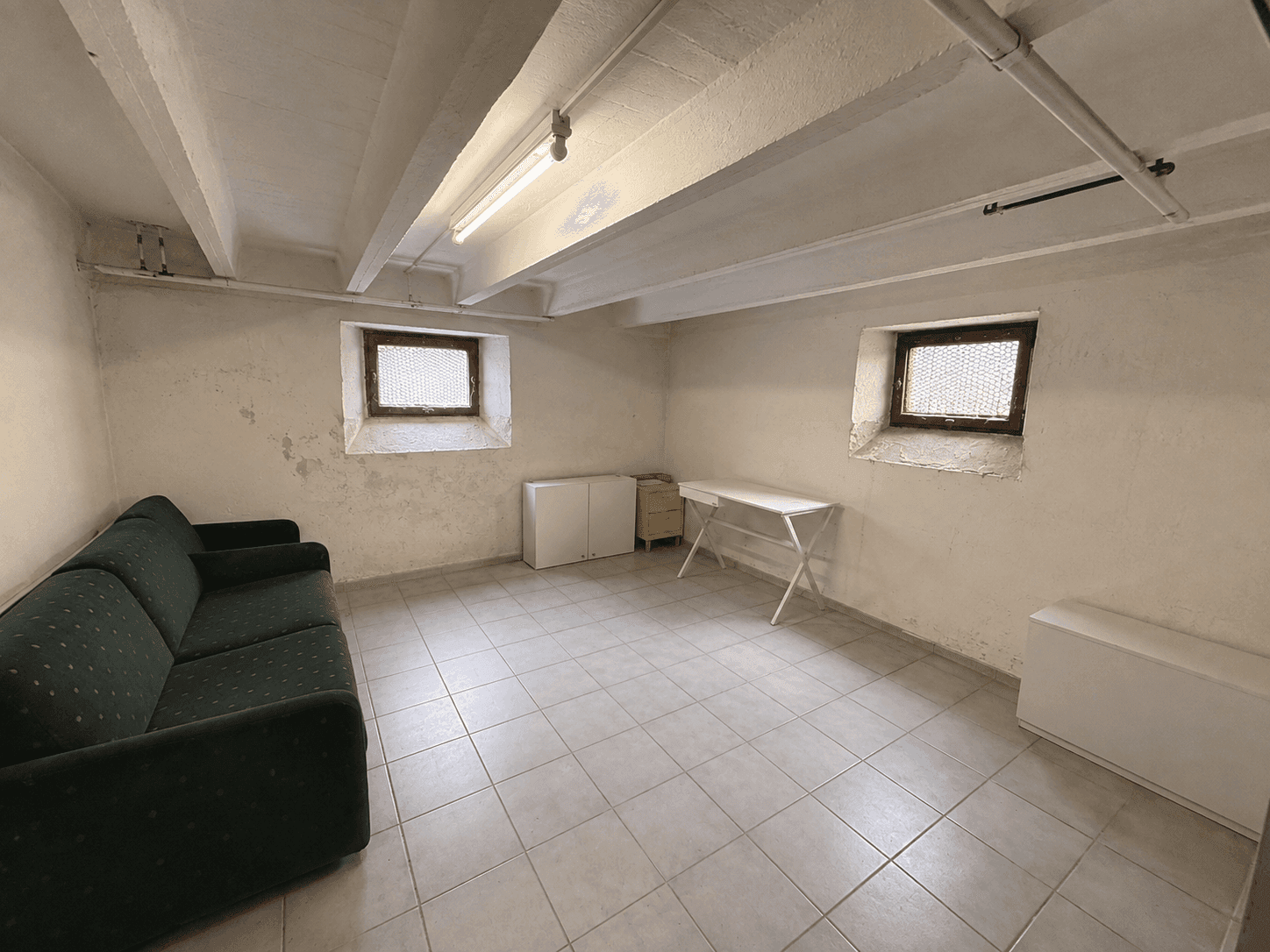 Ausgebauter Kellerraum mit Fliesenboden, Sofa und kleinen Fenstern.