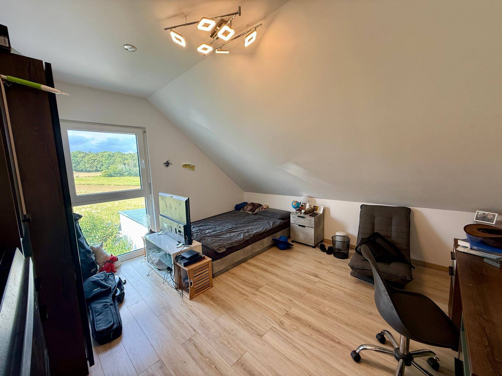 Jugendzimmer mit Bett, Schreibtisch und großem Fenster für viel Tageslicht.