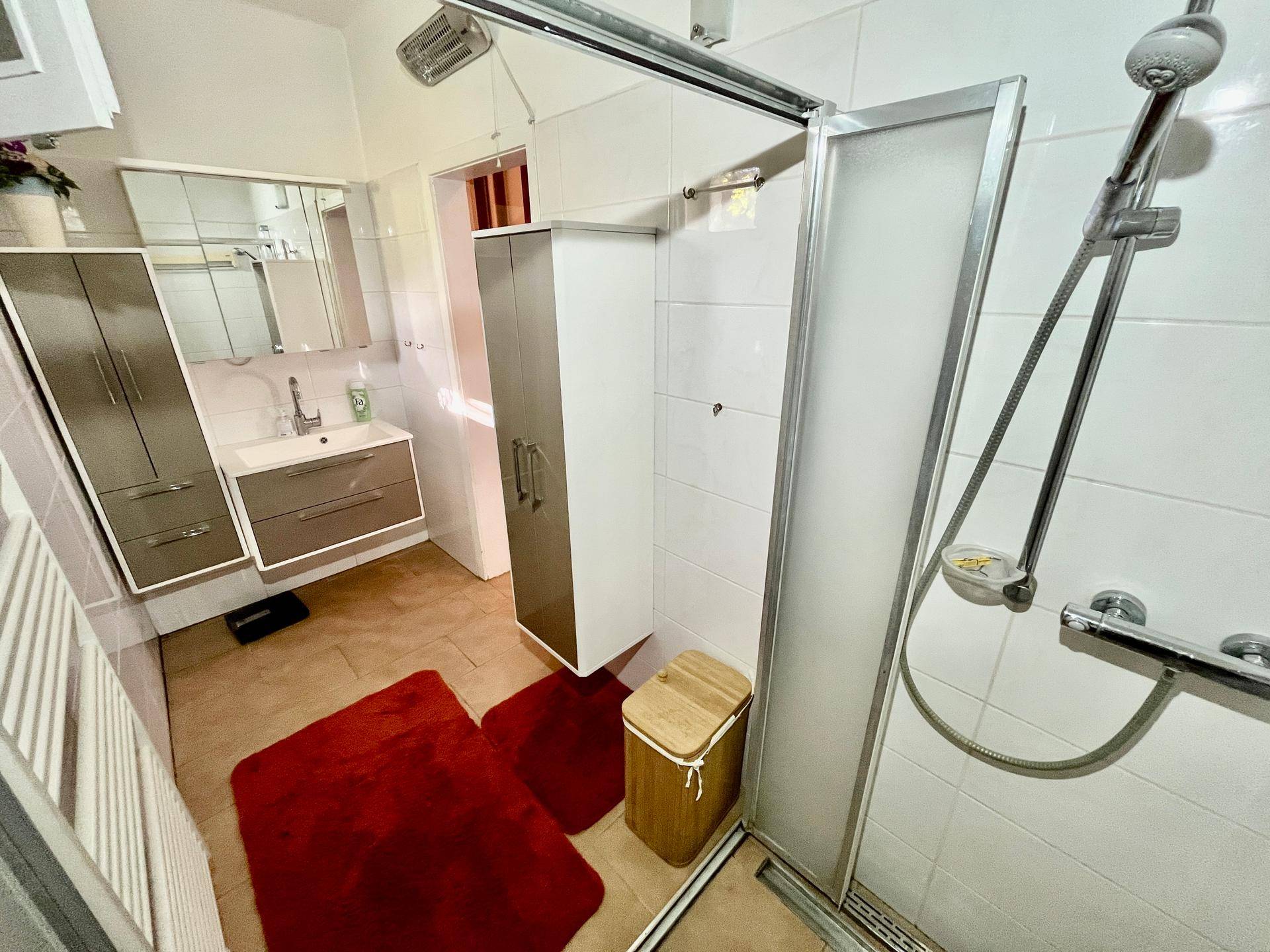 Modernisiertes Badezimmer mit Duschkabine, Waschtisch und hellen Fliesen.