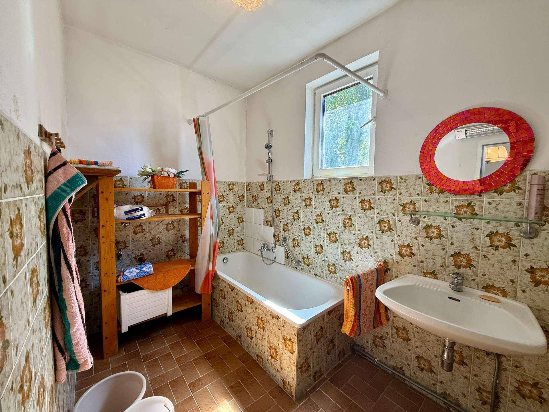 Badezimmer im 80er-Jahre-Stil mit Badewanne, Waschbecken und gemusterten Fliesen.