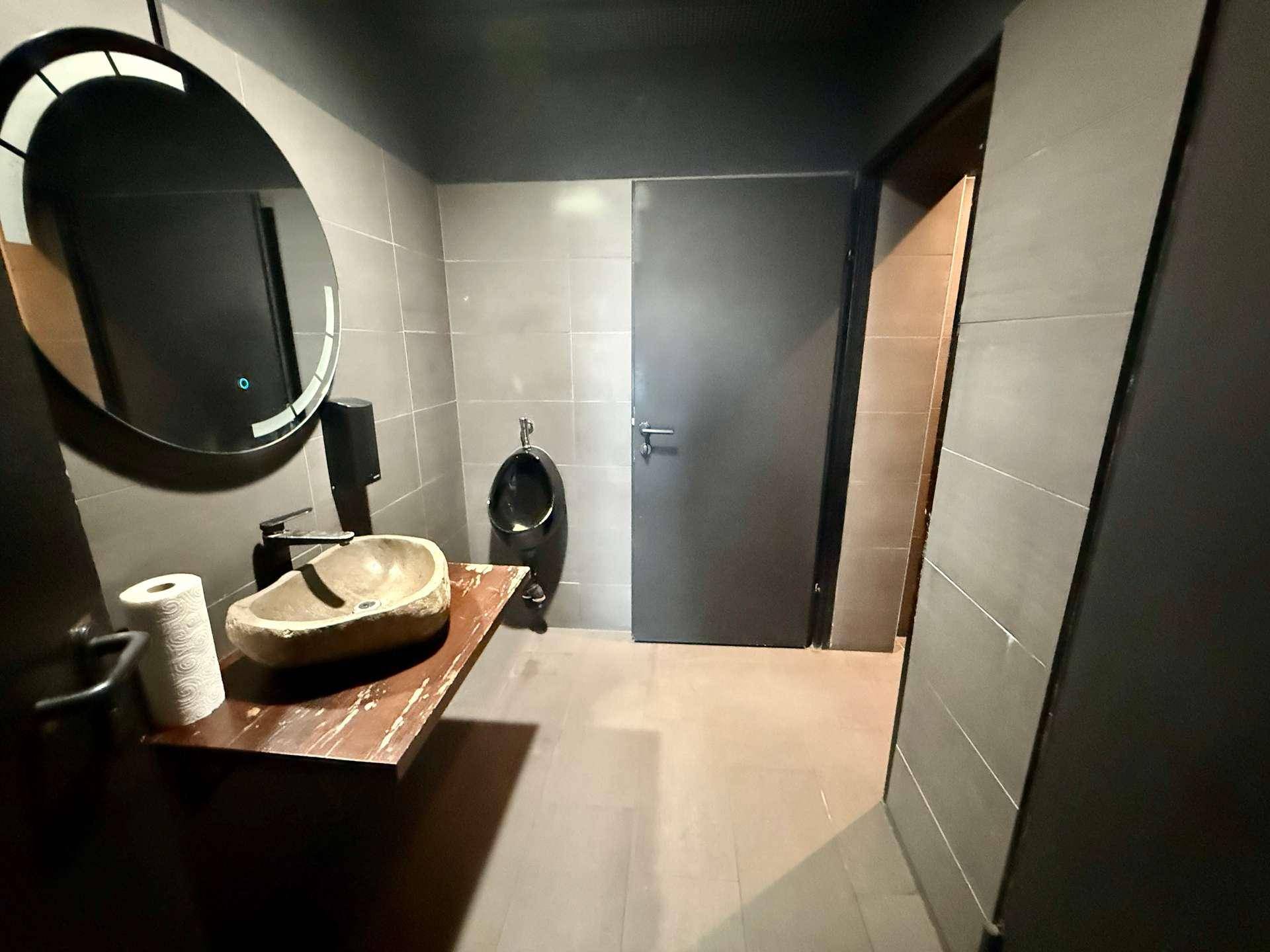 Badezimmer mit modernem Steinwaschbecken, Holzablage und einem Urinal, alles in dunklen Farbtönen gehalten.