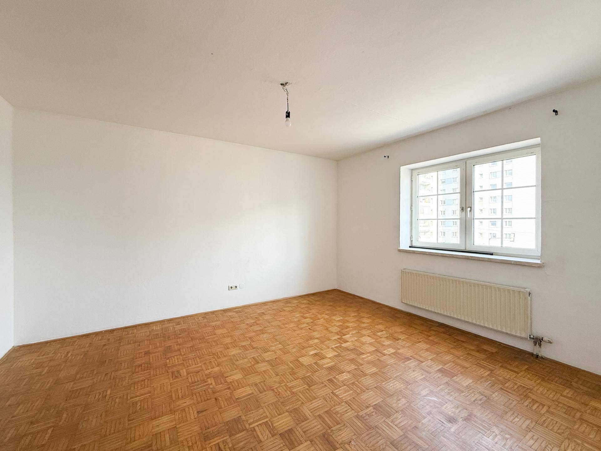 Geräumiges Wohnzimmer mit hellem Parkettboden und einem großen Fenster für natürliche Belichtung.