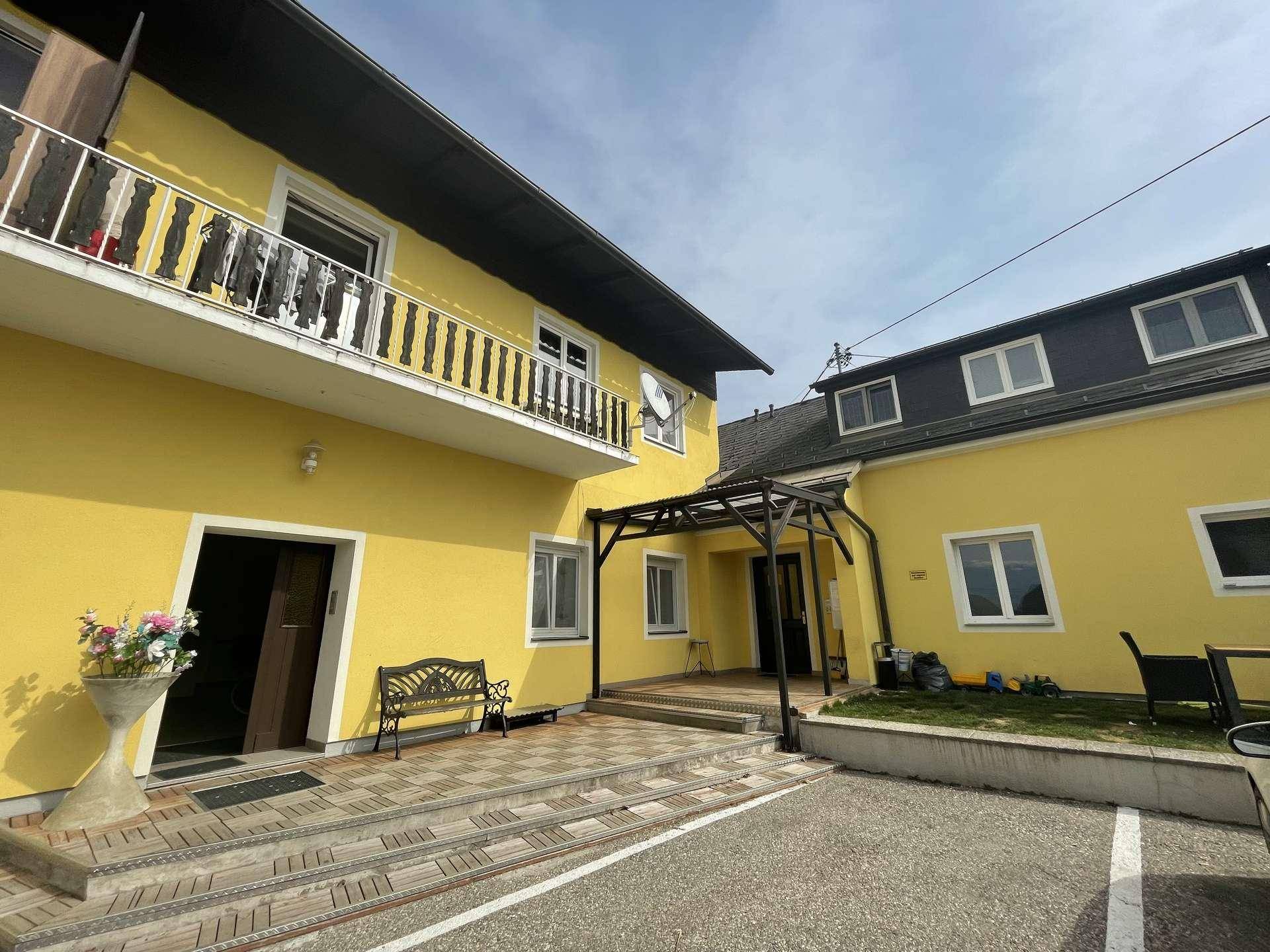 Gelbes Mehrfamilienhaus mit Balkon, überdachtem Eingangsbereich und gepflastertem Vorplatz.