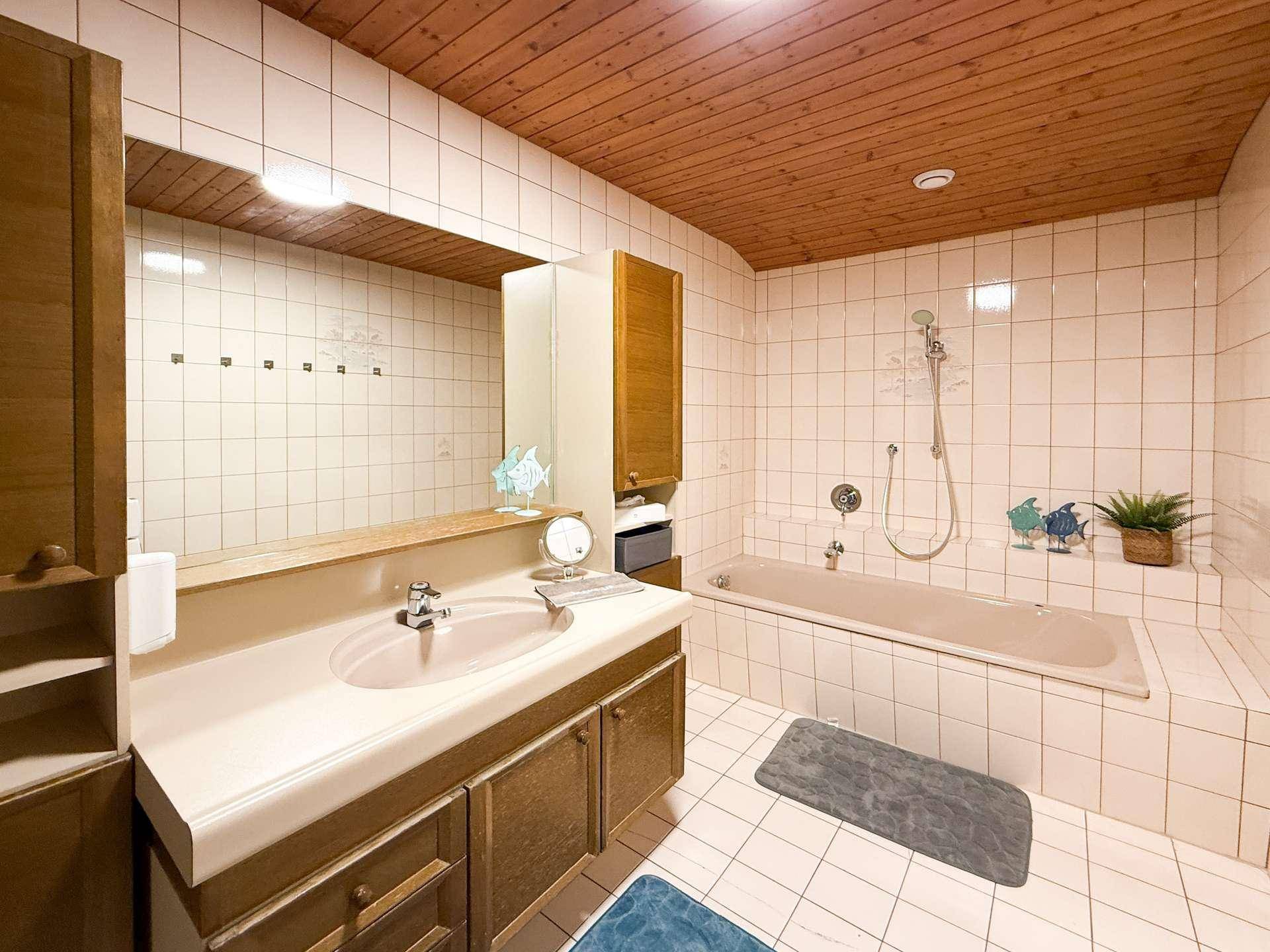 Geräumiges Badezimmer mit Badewanne, Waschtisch und Holzdecke.