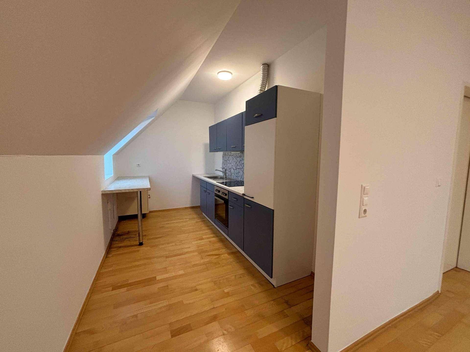 Kleine Einbauküche im Dachgeschoss mit blauen und weißen Schränken und Holzboden.